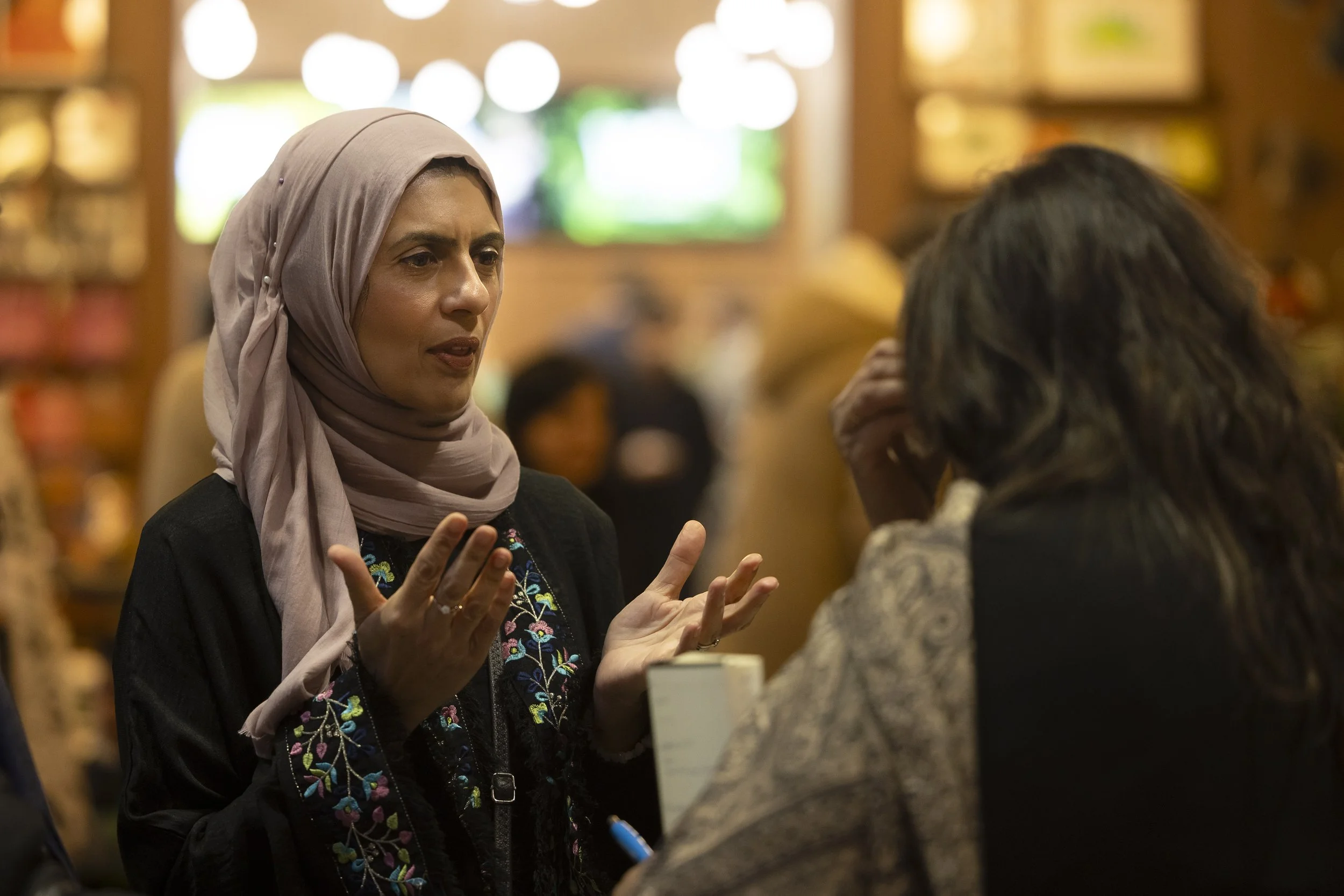 A woman wearing a hijab talks to another person while gesturing with her hands.