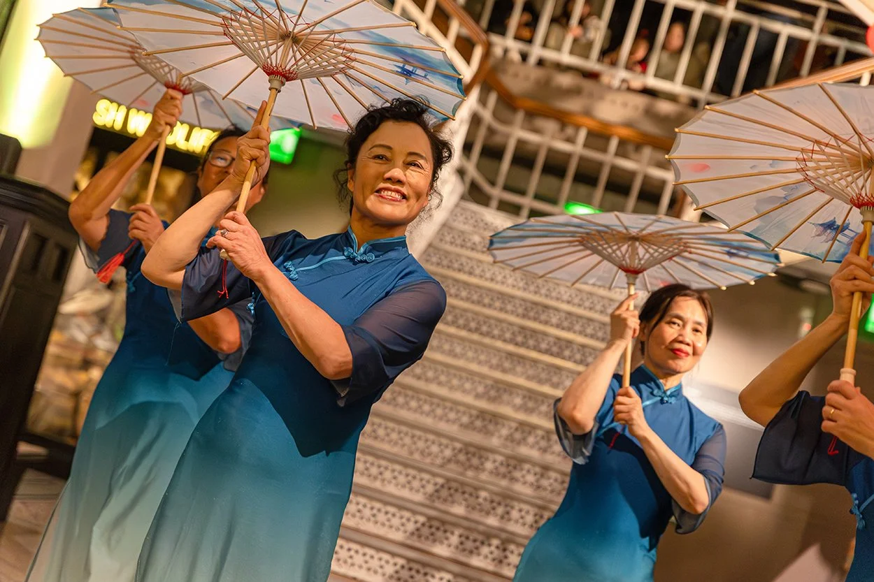 Women holding umbrellas and wearing traditional Chinese dress dance within Manchester Museum.