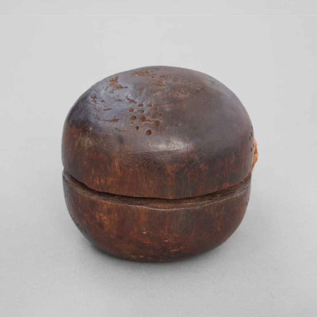 Wooden dog rattle with two peices of rope attached. There is a 'dot' pattern over the wood.