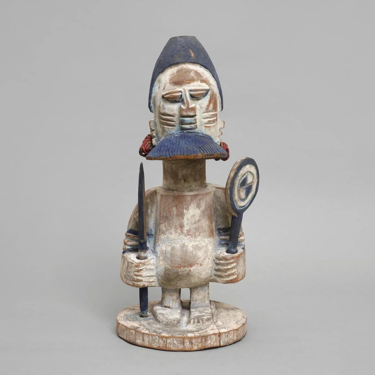 Carved wooden figure. A standing male figure holding a spear in his right hand and fan in his left.