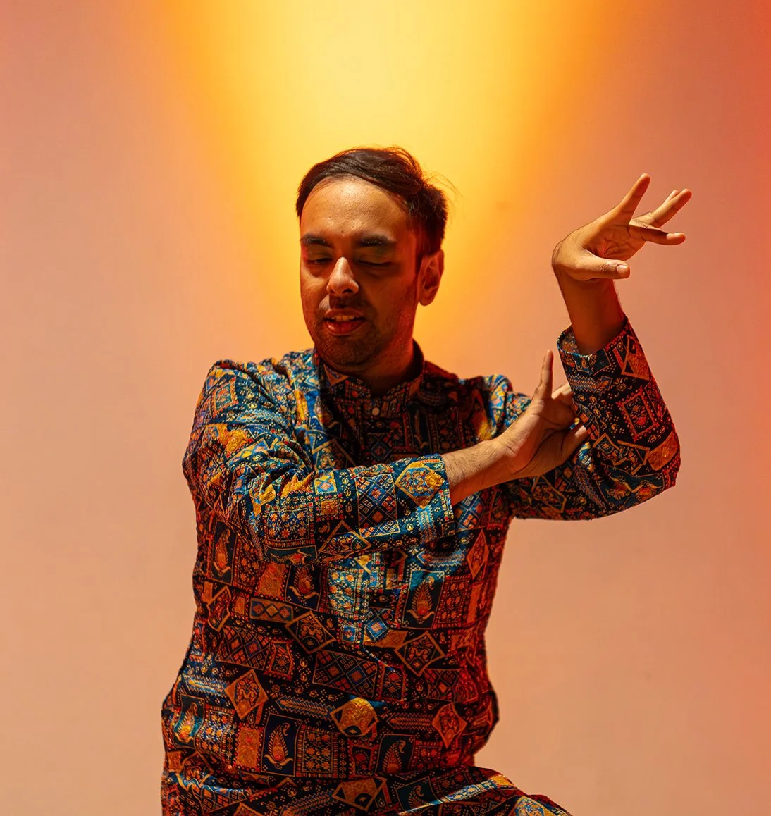 Person dancing with closed eyes, wearing colorful patterned shirt, against yellow and orange gradient background.