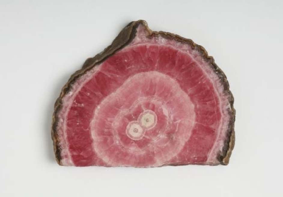 Slice of pink and brown mineral or gemstone, showing concentric bands and crystal formations.