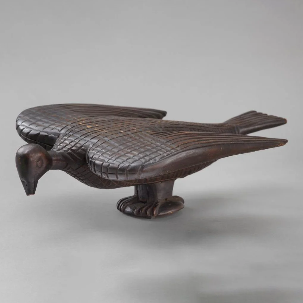 A wooden carving in the form of a pigeon with its wings half open. The object is carved from pale light wood and varnished brown.