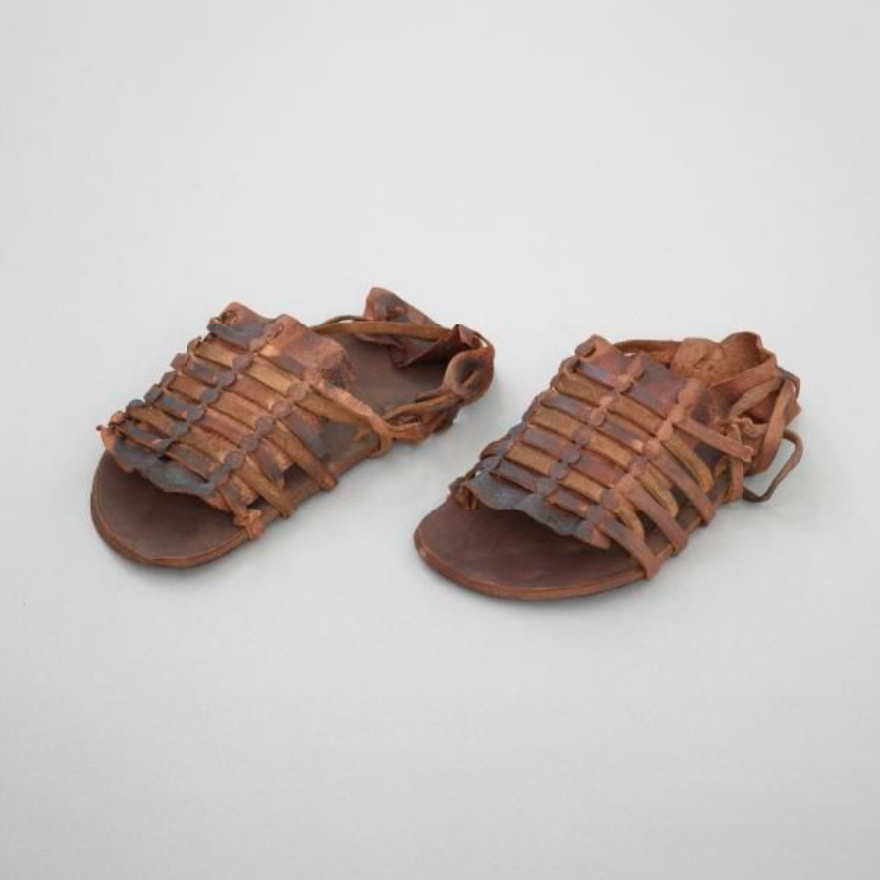 A pair of sandals. The soles are made of thick leather, the uppers of thinner leather straps, threaded through a panel of leather.