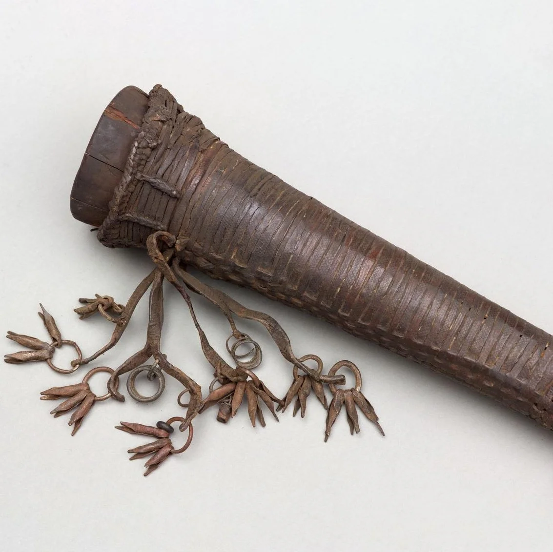 A horn consisting of a wooden tube wrapped in leather strips. There are a bunch of iron rattles at the wider end.