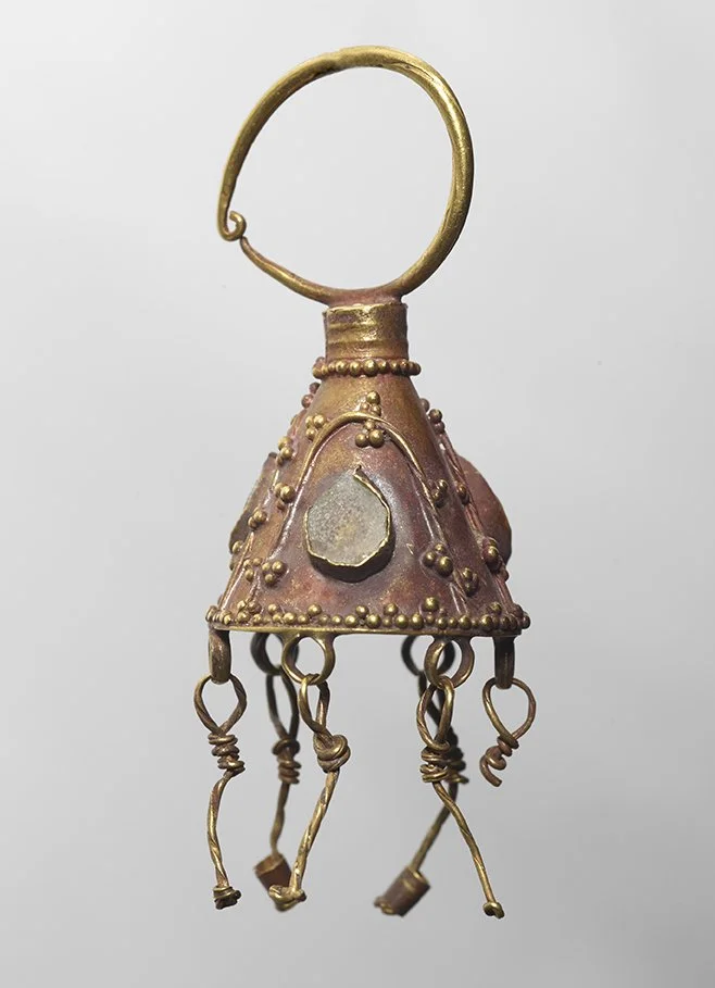 A small decorative bell with a gold handle and hanging metal loops, adorned with tiny beads and raised designs, in a reddish-brown color.