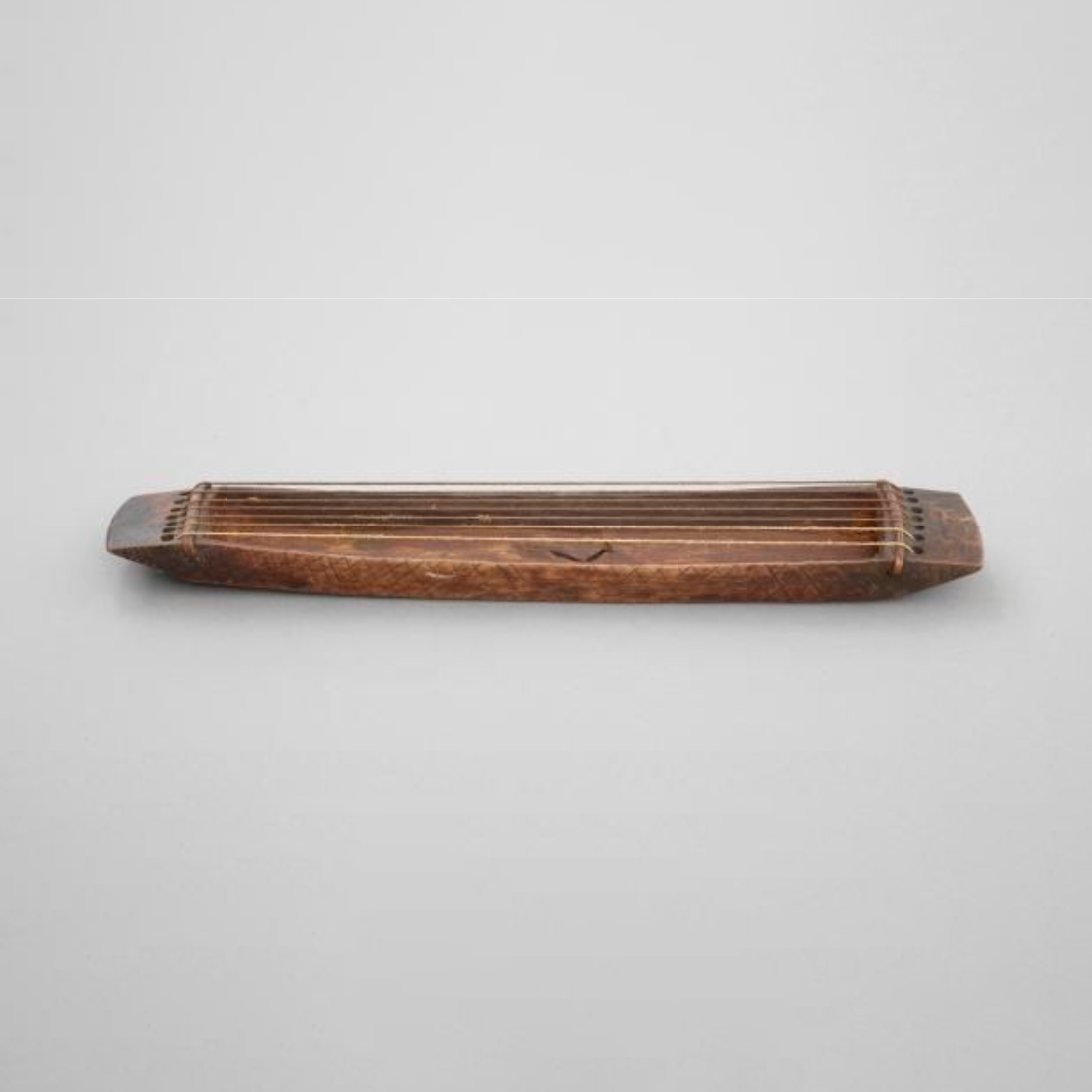 This is a stringed musical instrument. The base is a hollow rectangle of wood with a pierced lug at either end, between which are stretched seven fibrous strings.