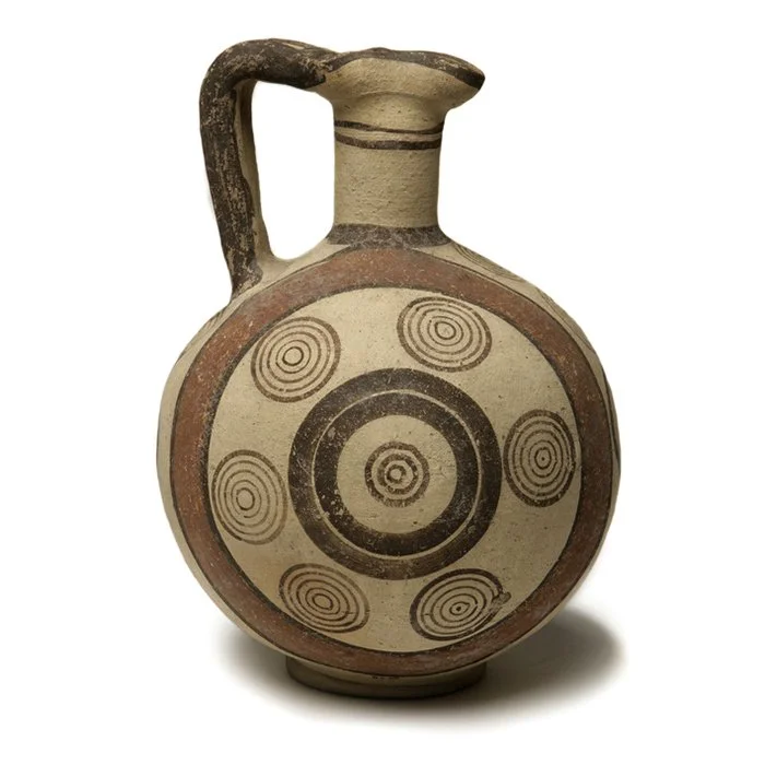 Ancient ceramic vessel with a round body, a small handle on the top, and a decorated geometric pattern of concentric circles in brown and black on a beige background.