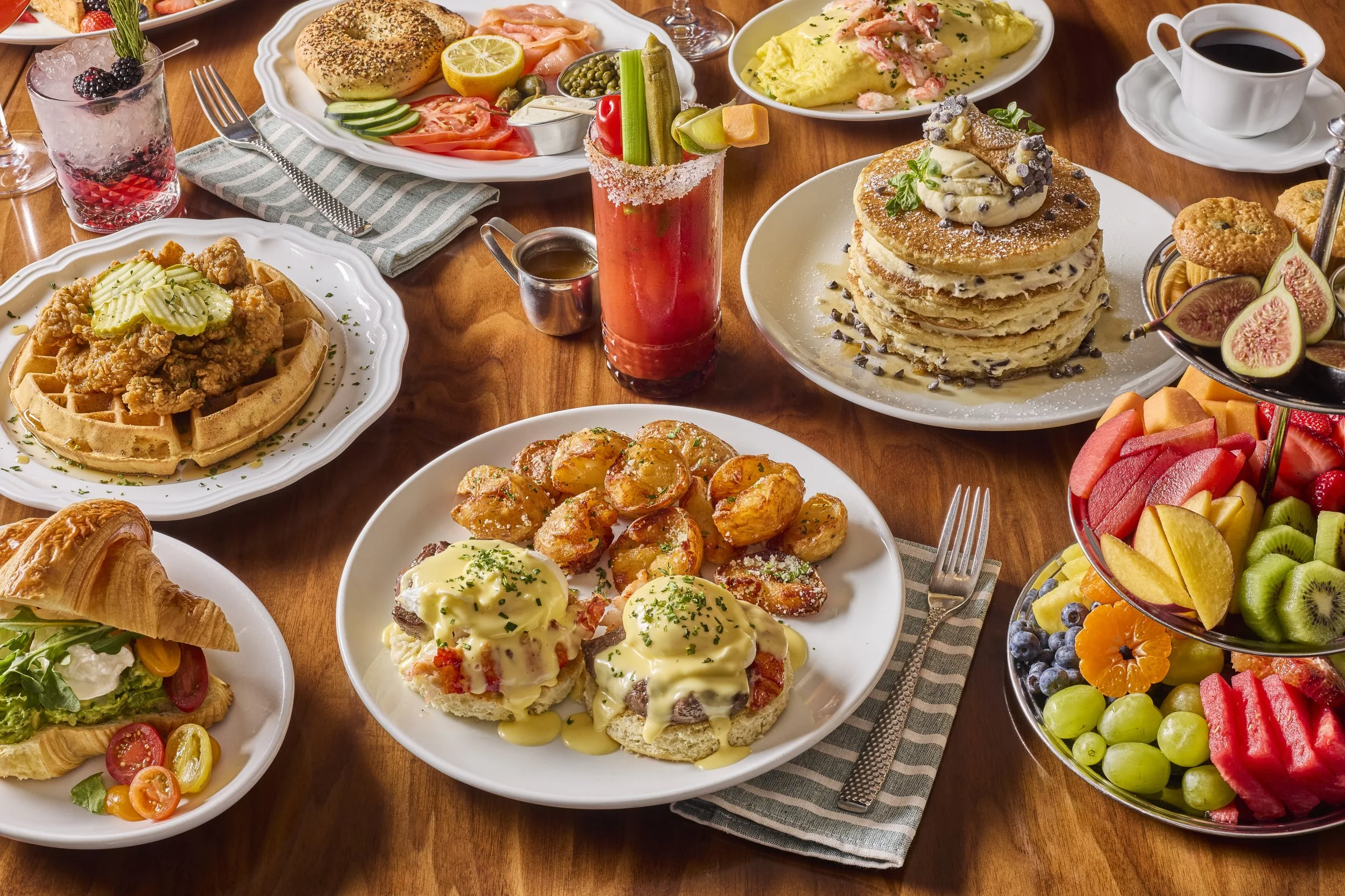 A table filled with various breakfast dishes including pancakes, scrambled eggs, fried chicken and waffles, fruit, and beverages.