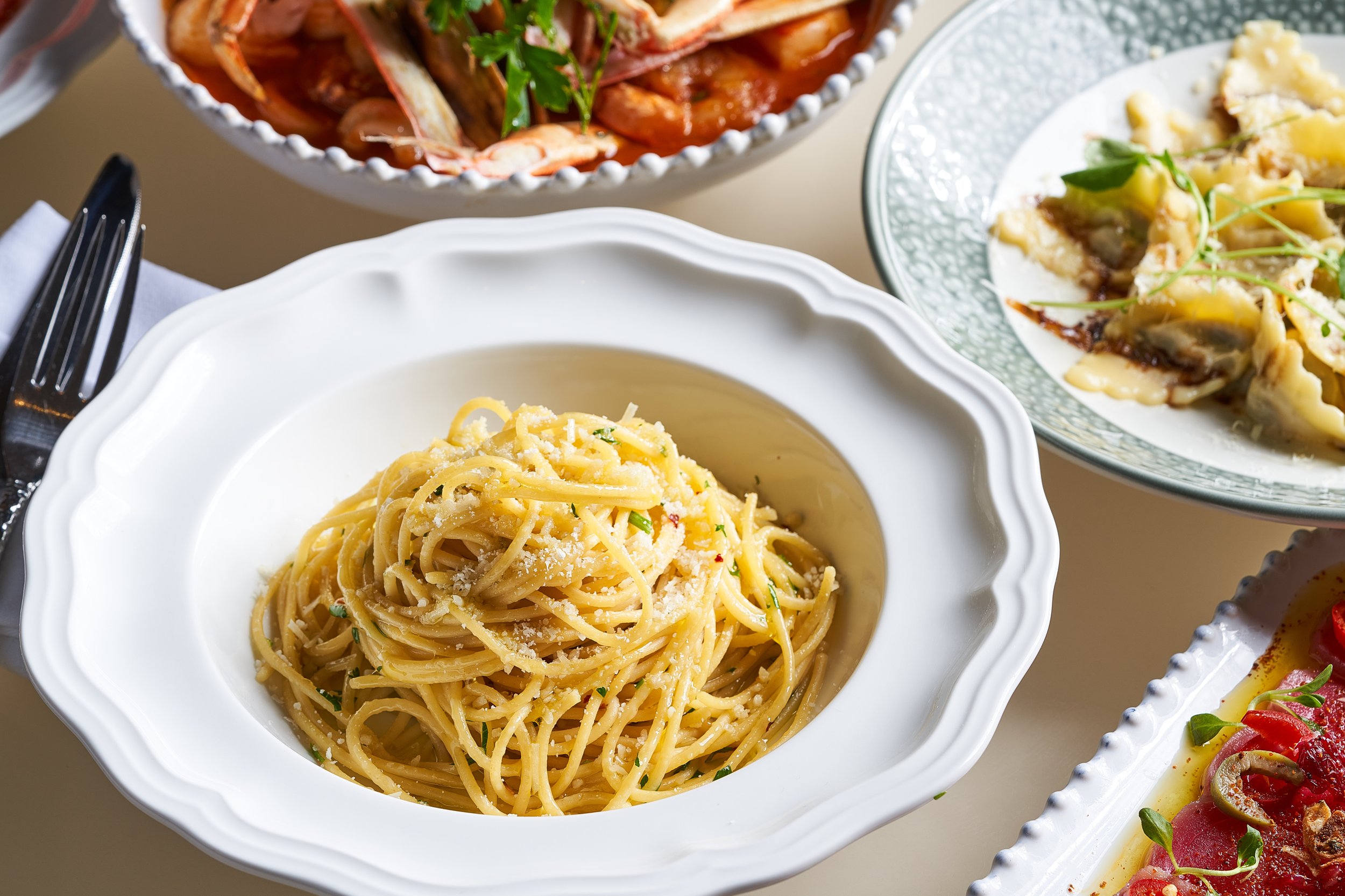 A plate of spaghetti pasta garnished with grated cheese and herbs, with other dishes of food partially visible.