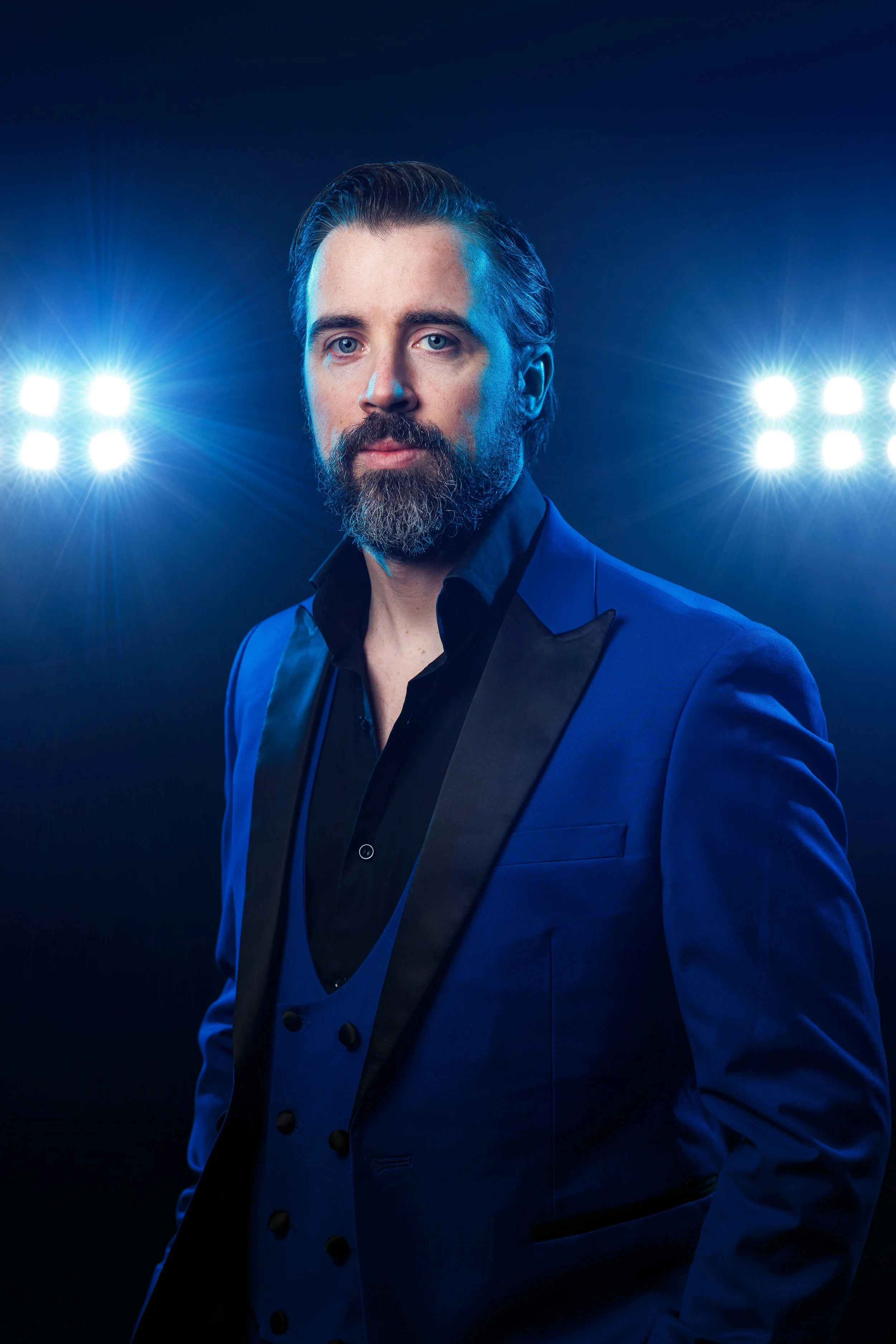Portrait of a bearded man wearing a plaid shirt against a dark background.