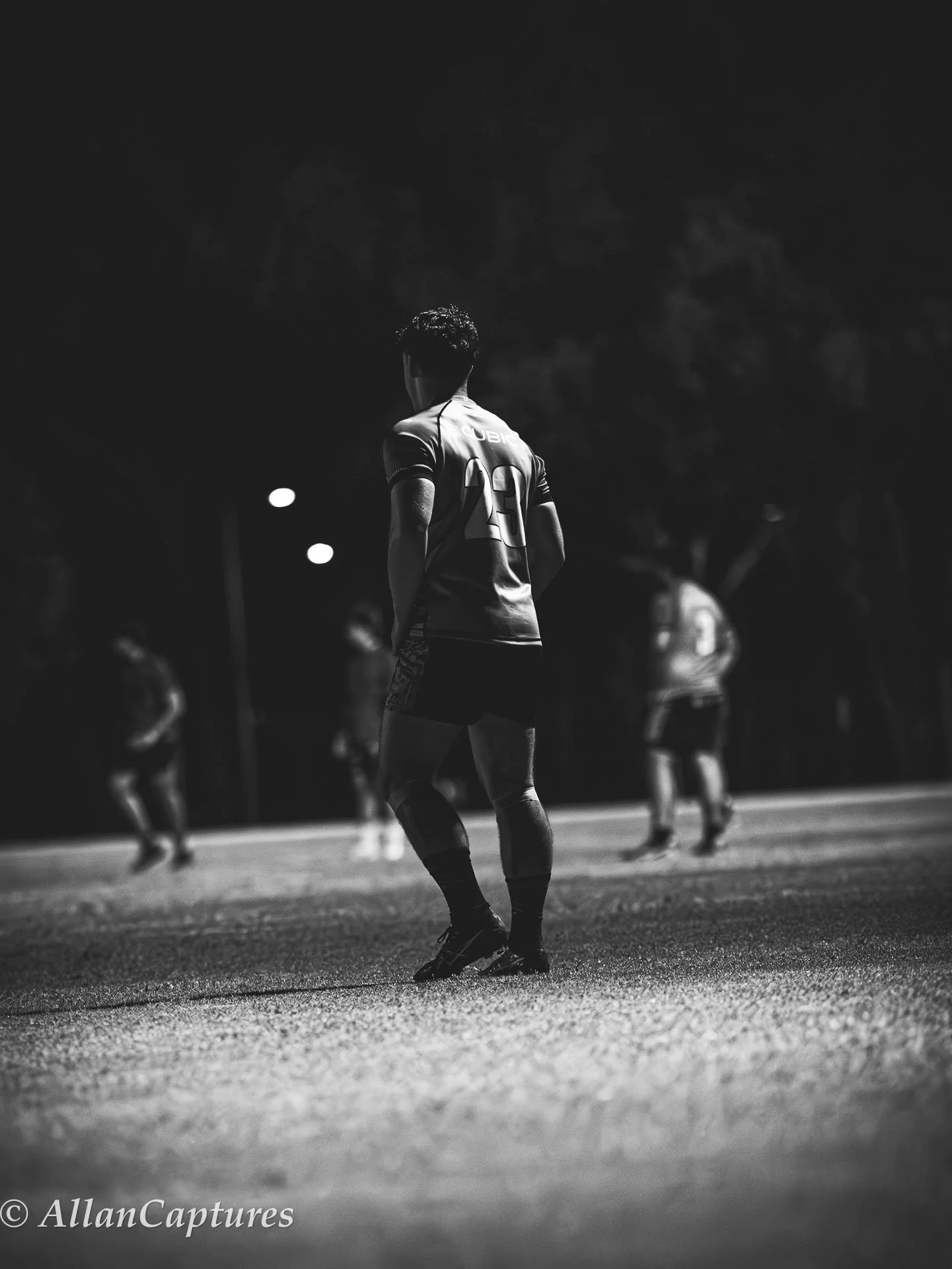A black and white photo of a rugby player with the number 23 on his jersey standing on the field, with other players visible in the background.