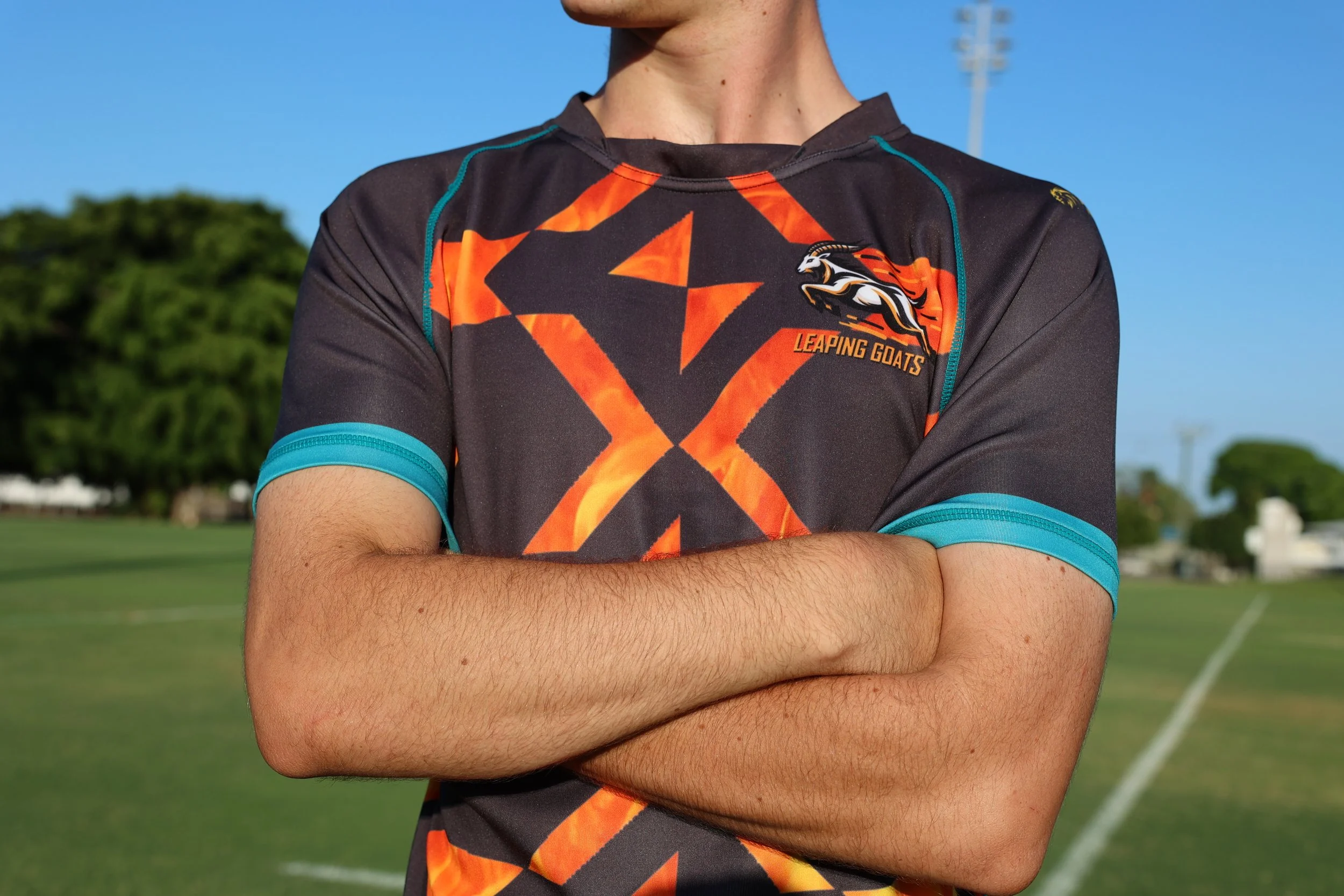 Close-up of a person wearing a uniform with a logo that says 'Leaping Goats' on a sports field.