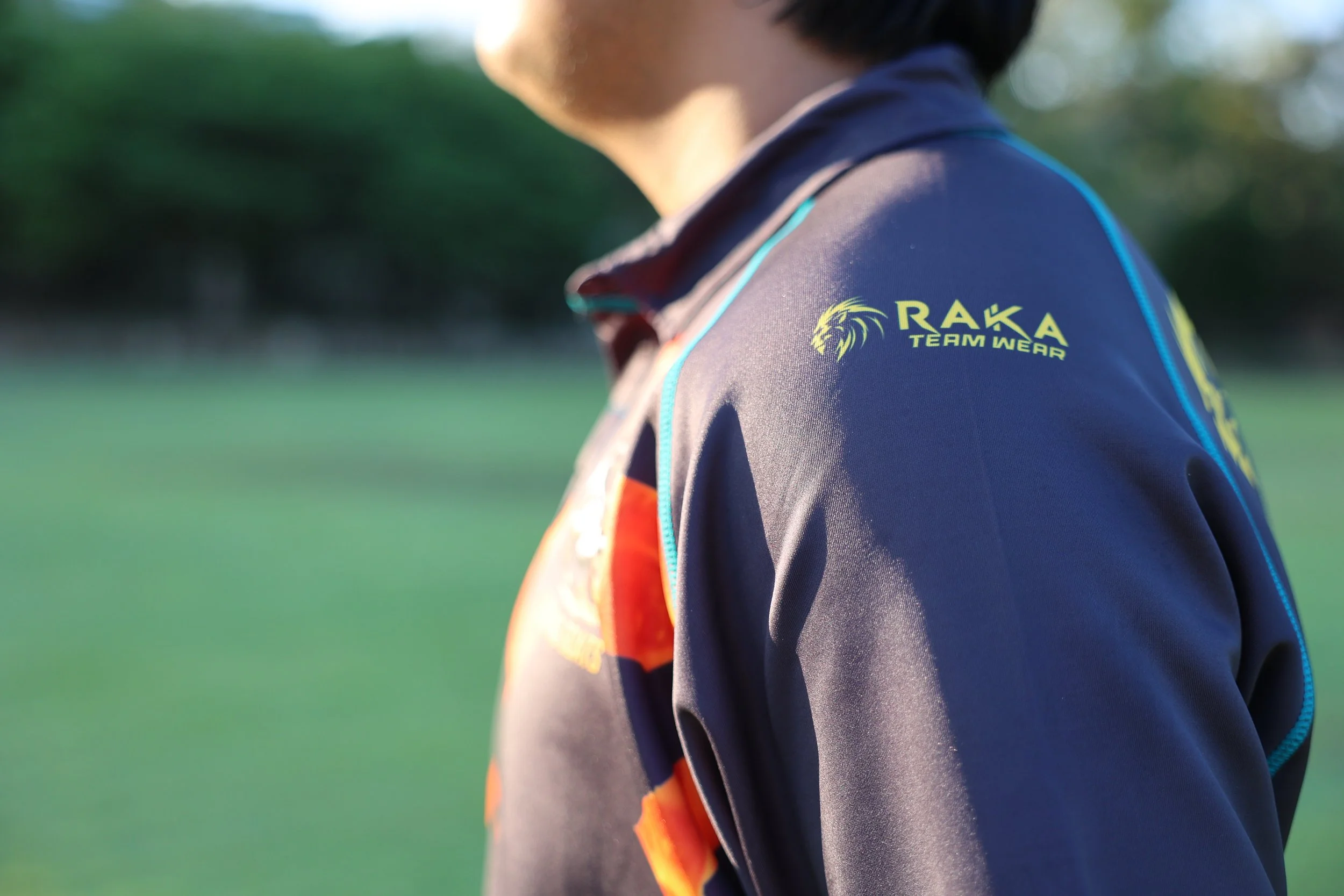 Close-up of a person wearing a dark sports jacket with the logo "RAKA TEAM WEAR" on the shoulder.
