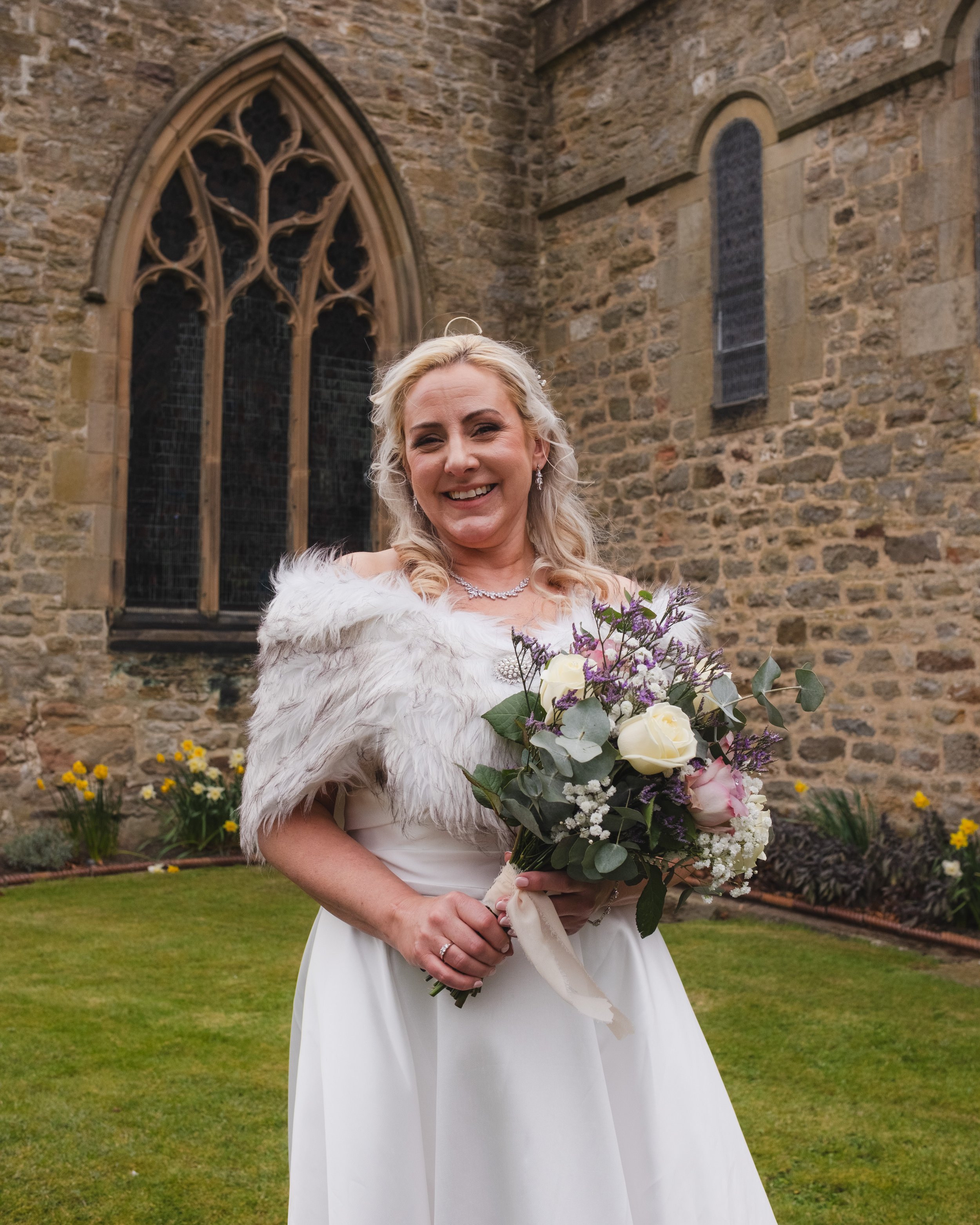 Bride holding a bouquet in front of a stone church building.