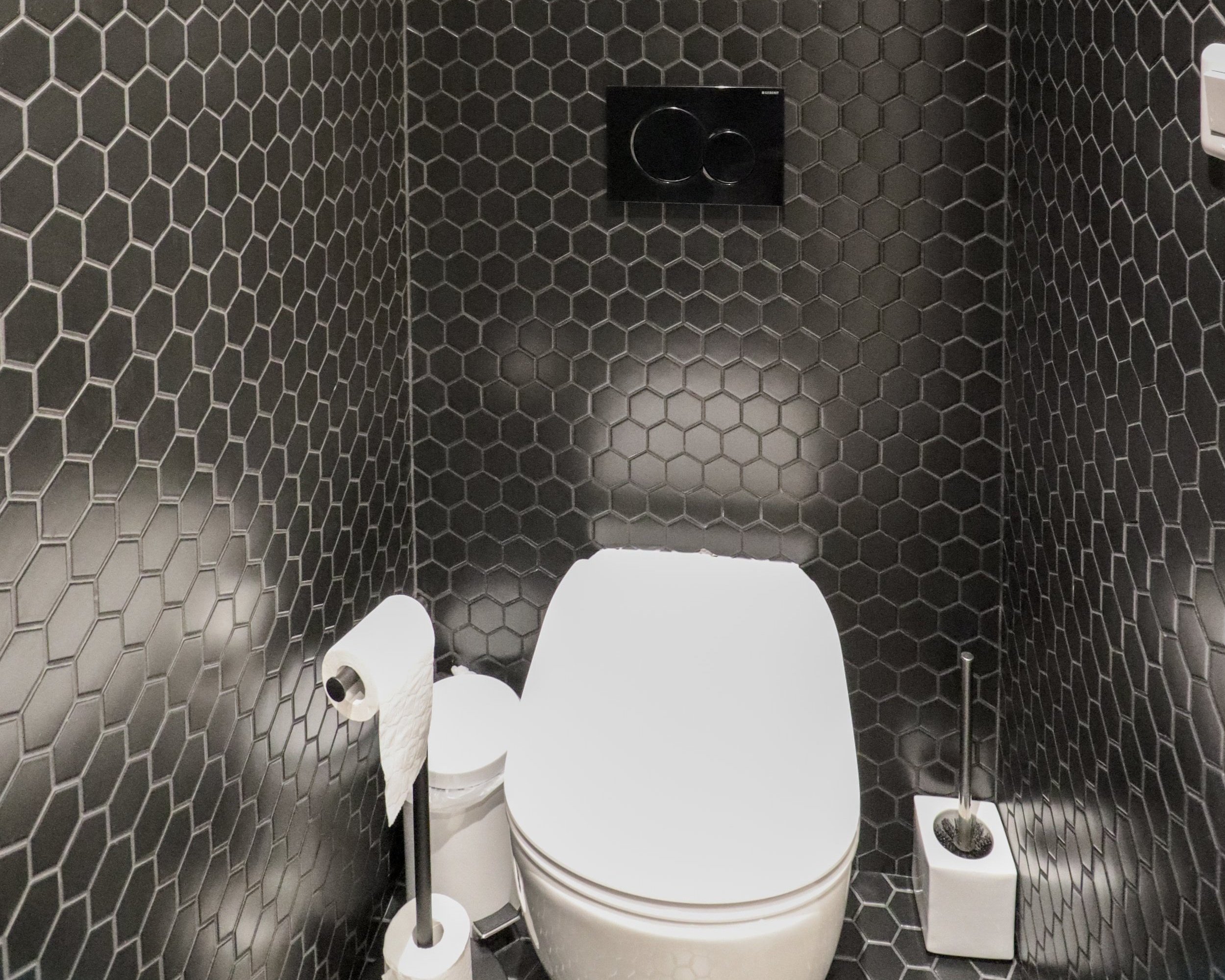 Toilettes avec murs en carrelage hexagonal noir et accessoires en acier inoxydable.