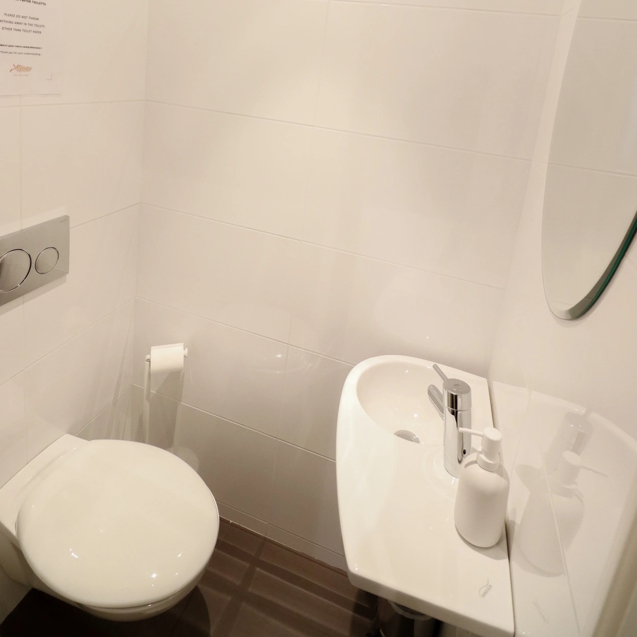 Une salle de bain avec un lavabo blanc, un miroir, un porte-serviette et un papier hygiénique.