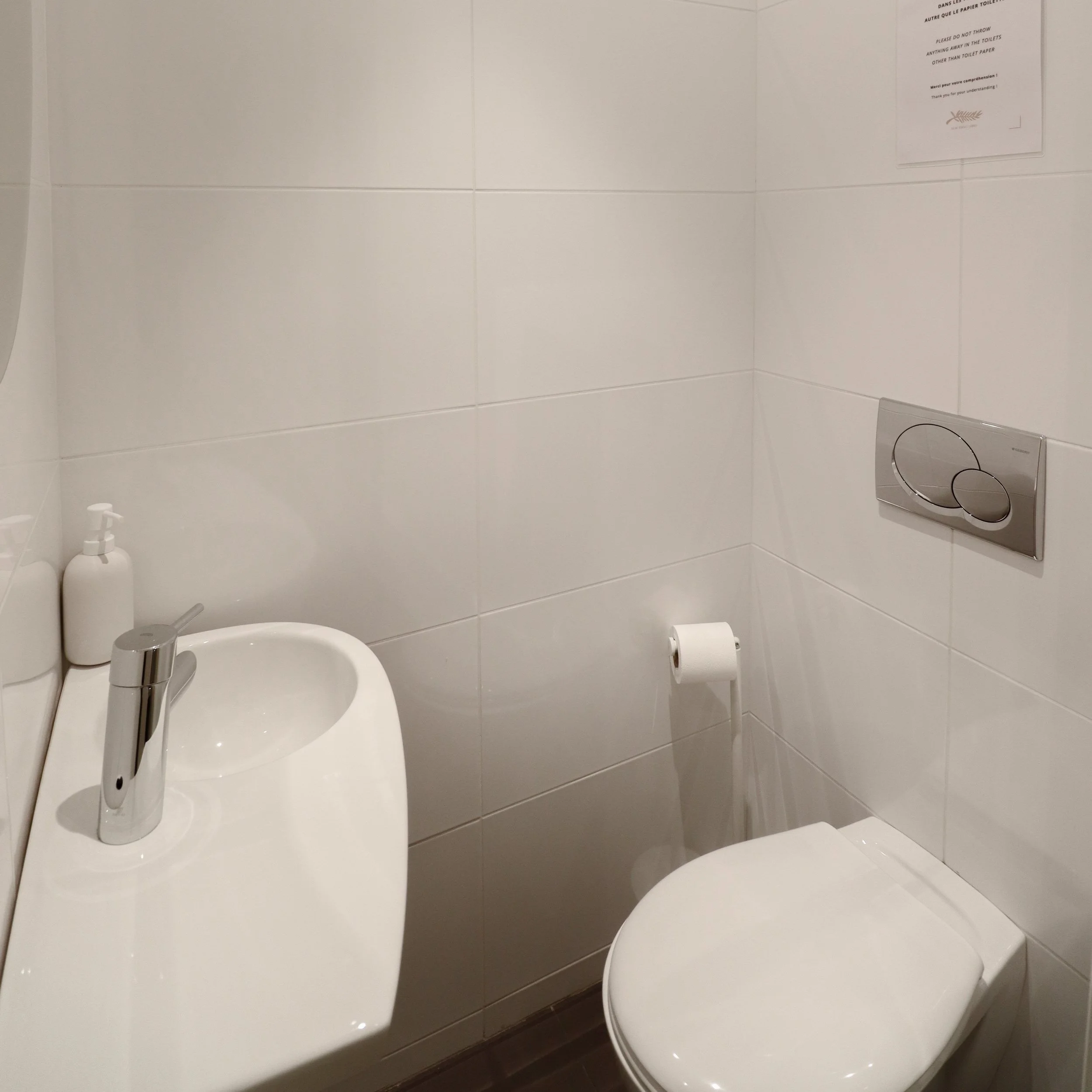 Vue partielle d'une salle de bain avec un lavabo, un miroir et un panneau avec des instructions en français et en anglais au mur.