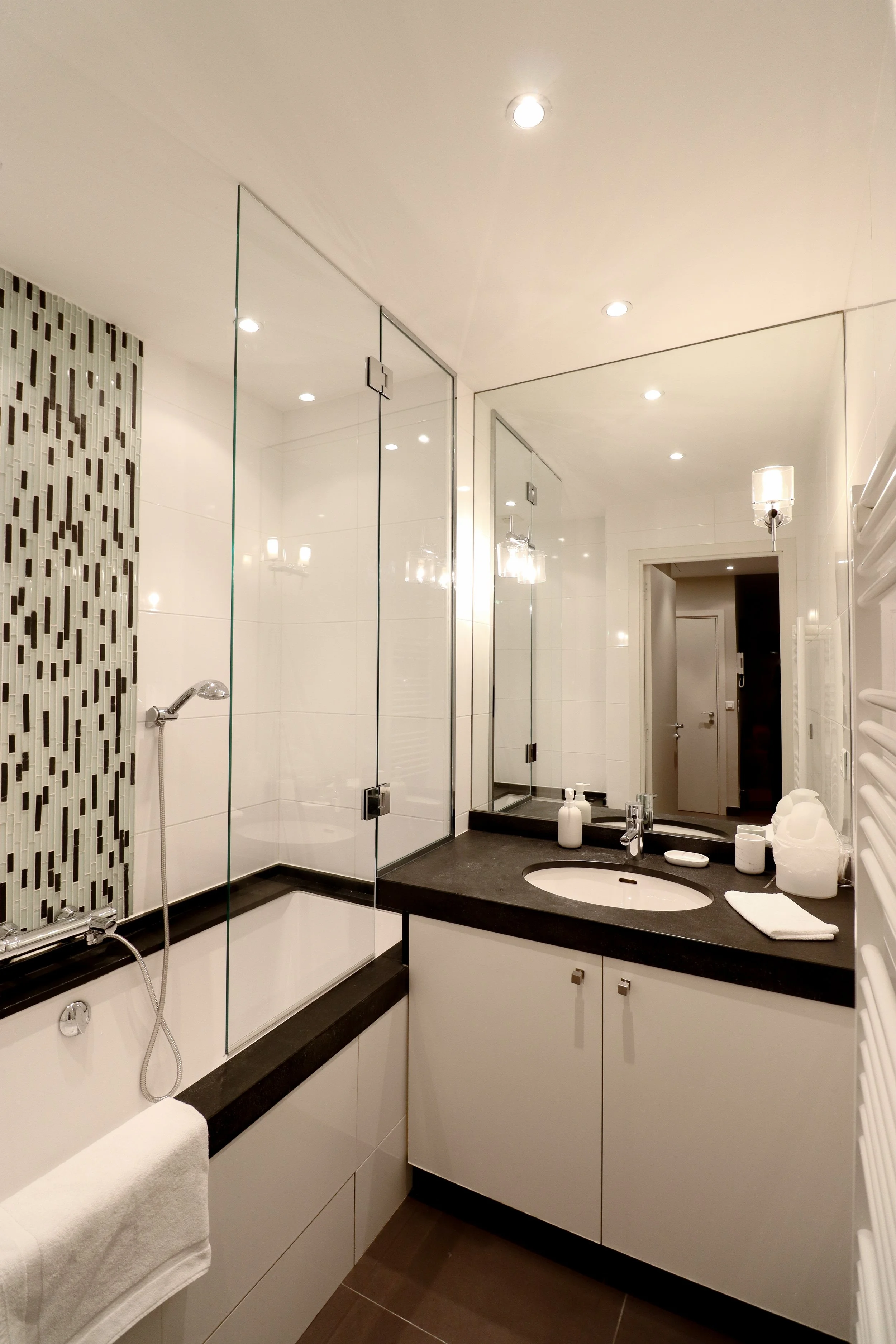 Une salle de bain moderne avec une douche en verre, un lavabo intégré dans un meuble clair, un miroir, des lampes suspendues au plafond, des toilettes, et des accessoires de toilette blancs. La décoration se veut épurée et élégante.