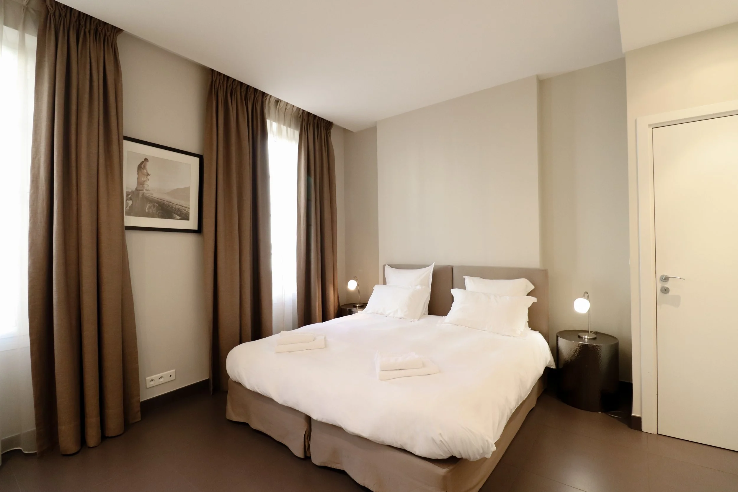 Chambre d'hôtel avec un lit blanc, des rideaux marron et un tableau d'art au mur.
