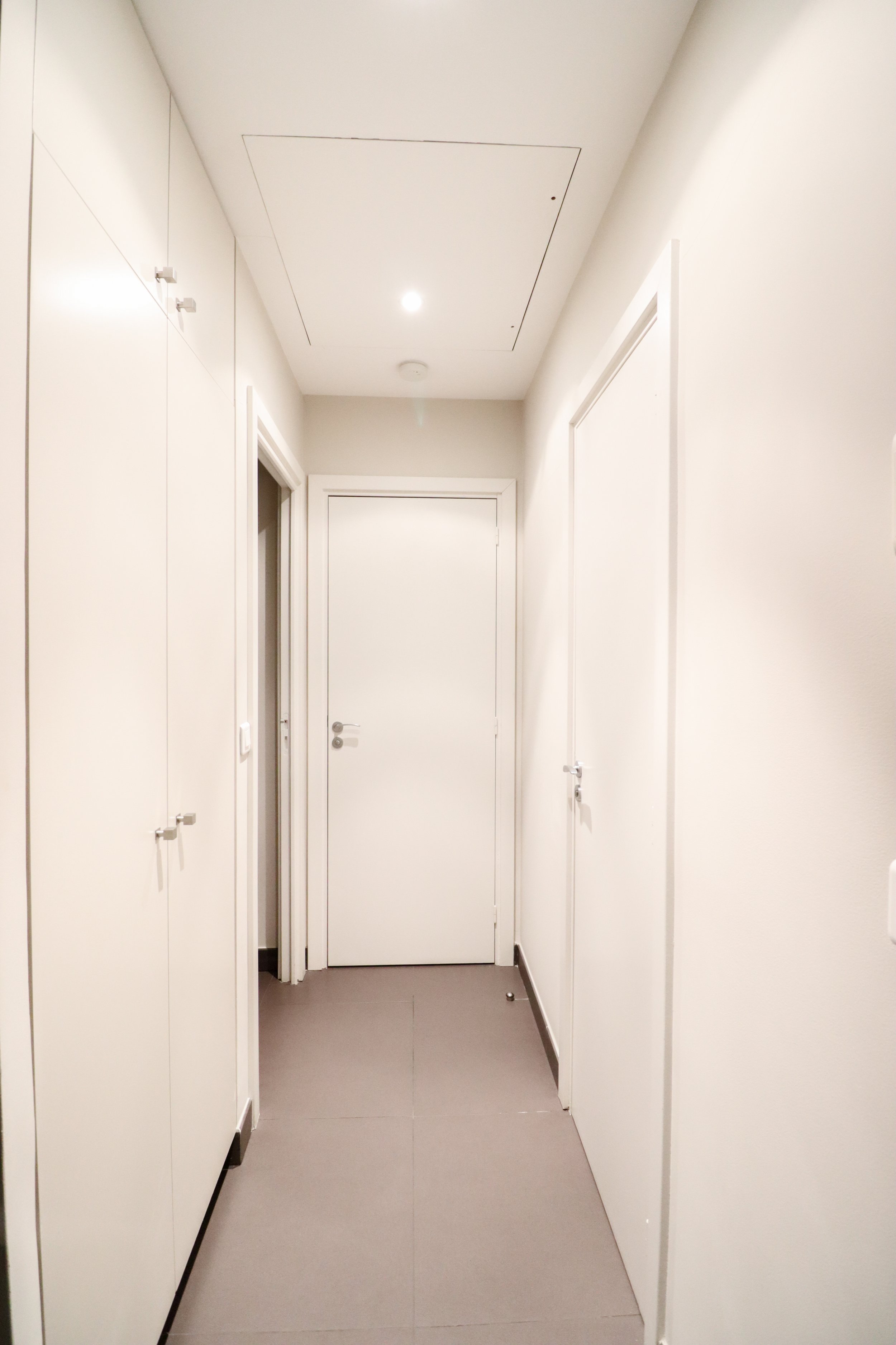 Couloir blanc avec armoires de rangement sur les côtés et une porte blanche à l'extrémité.