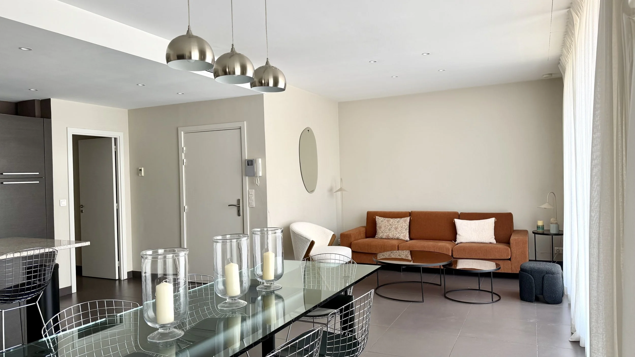 Salon moderne avec canapé orange, table basse ronde, et mur blanc, éclairé par des lampes suspendues en métal et des petites lumières encastrées au plafond.