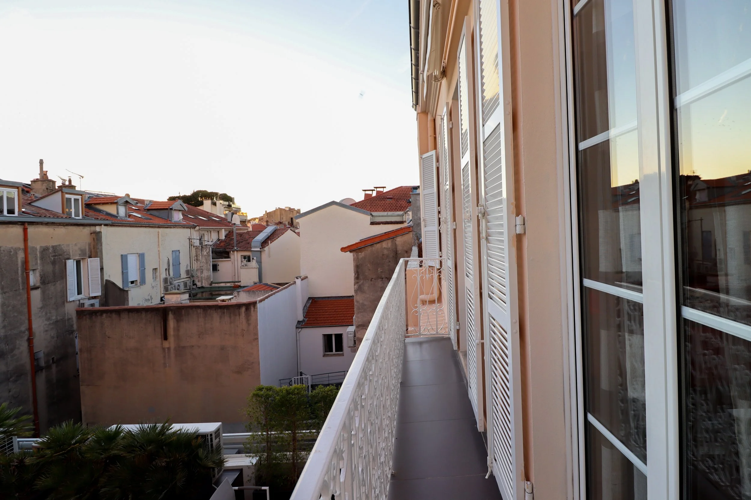 Balcon vu sur un quartier résidentiel avec maisons aux toits en tuiles rouges, fenêtres avec volets, au crépuscule.