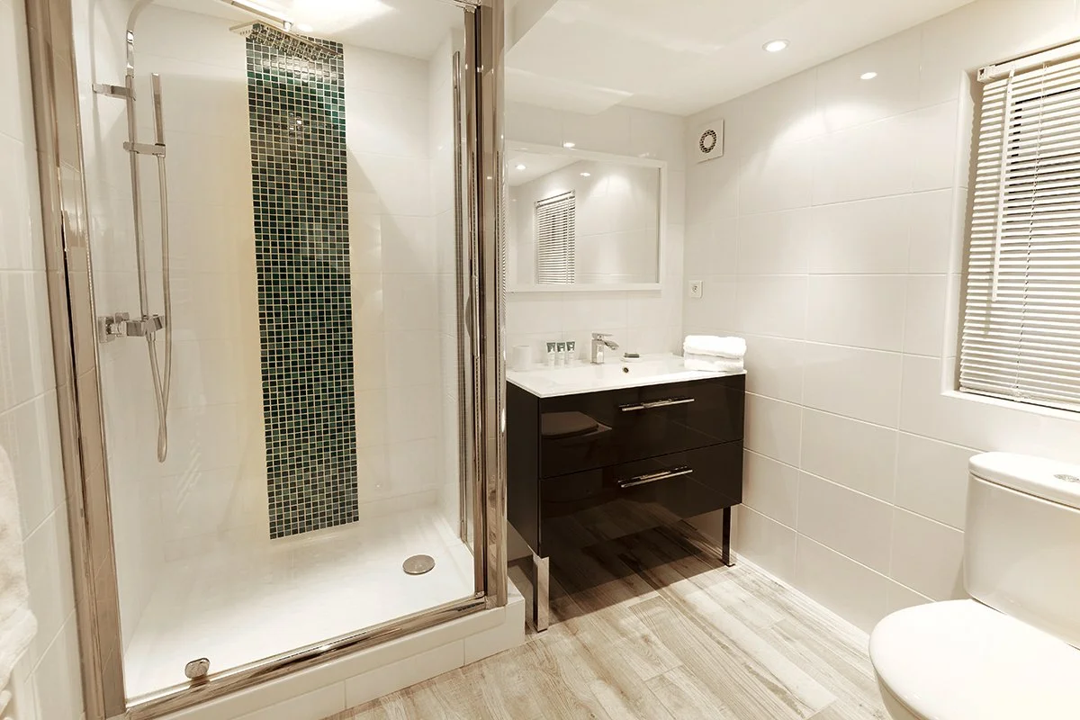 Salle de bain moderne avec cabine de douche en verre, lavabo avec miroir, toilettes et fenêtre avec stores