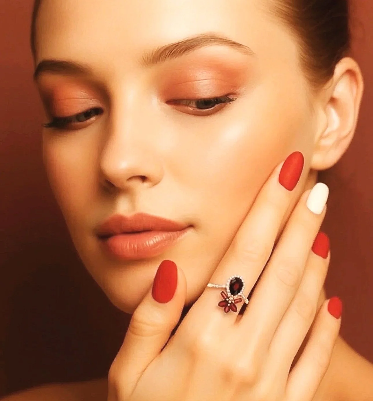 Close-up of a woman with natural makeup, red and white painted nails, and a floral ring on her finger.