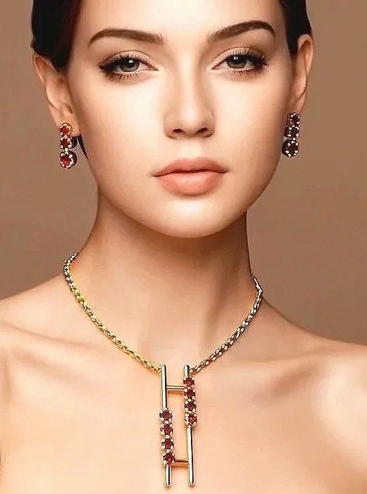 A woman with a neutral expression wearing earrings and a gold necklace with red gemstones and gold bars.