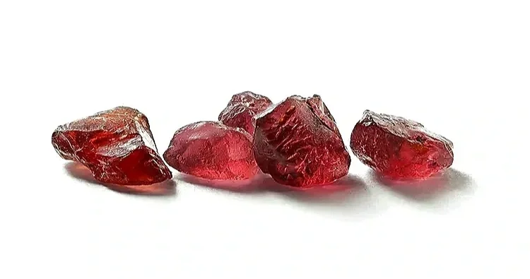 Five raw, uncut red gemstones or rubies placed on a white background.