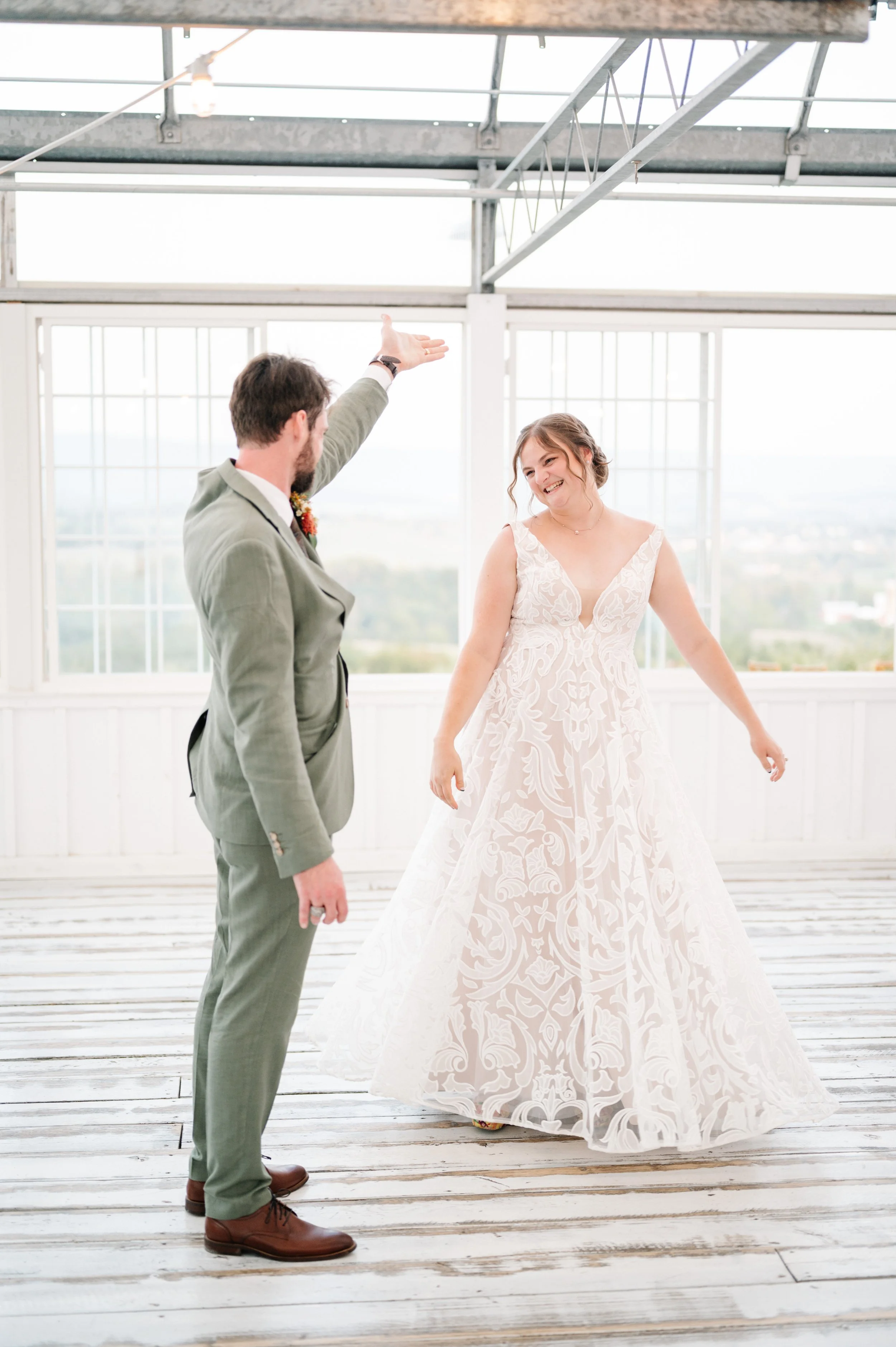 A bride and groom dancing inside a bright, airy room with large windows, white walls, and a wooden floor.