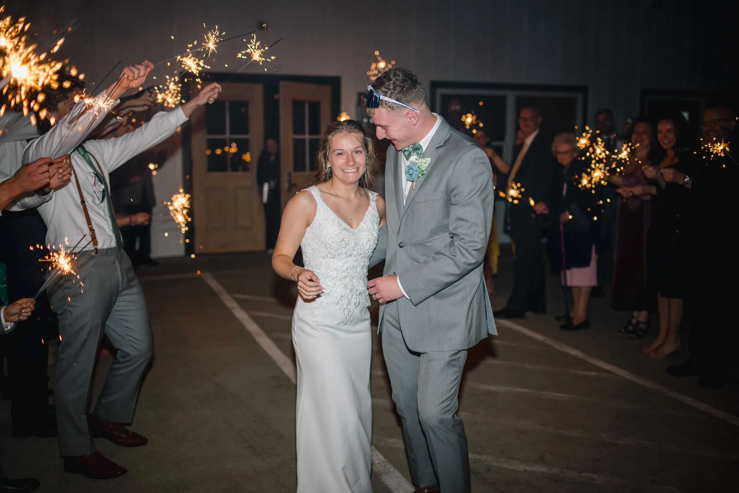 Bride and groom dancing at their wedding reception surrounded by friends holding sparklers at night