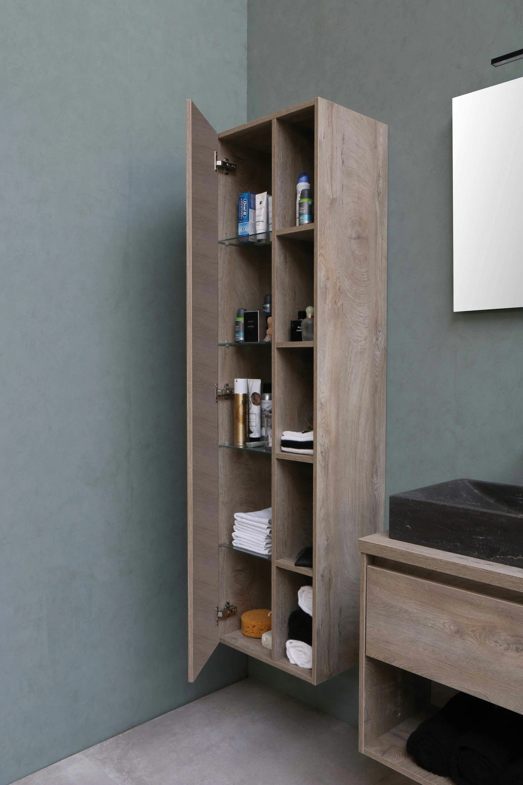 Tall wood bathroom storage cabinet with the door open, showing shelves stocked with toiletries, folded towels, and rolled washcloths.