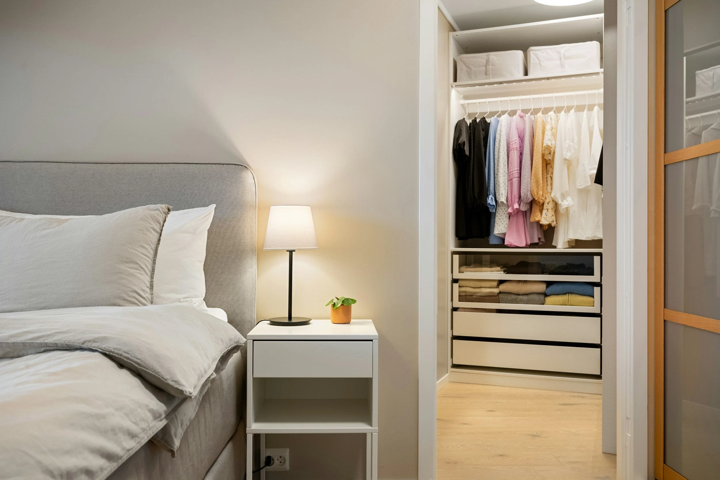 Neatly organized master closet with hanging clothes and drawer storage beside bedroom in a St. Louis home