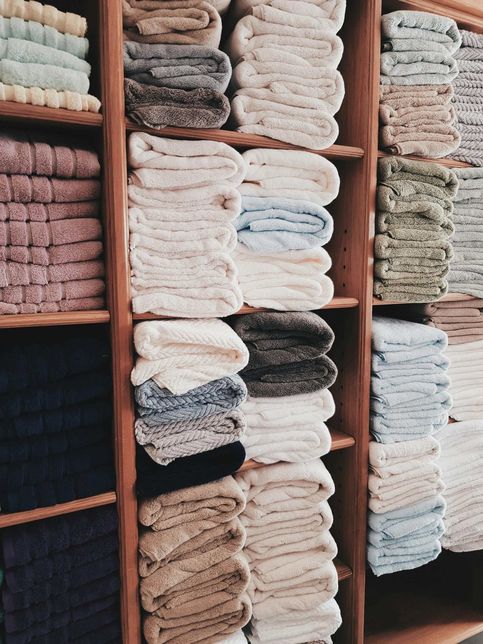 Professionally organized linen closet with neatly folded towels arranged by color on wooden shelves in a St. Louis home
