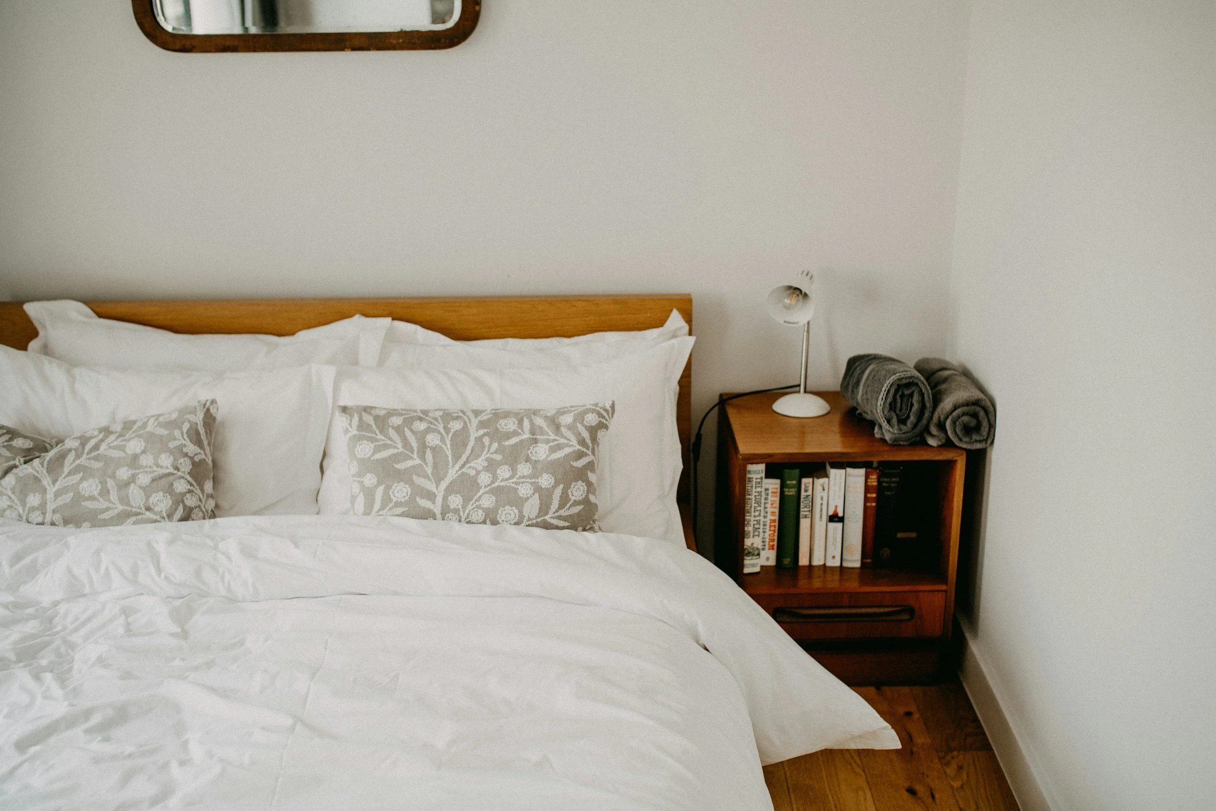Organized guest bedroom with nightstand storage, neatly arranged books, and rolled towels in a St. Louis home