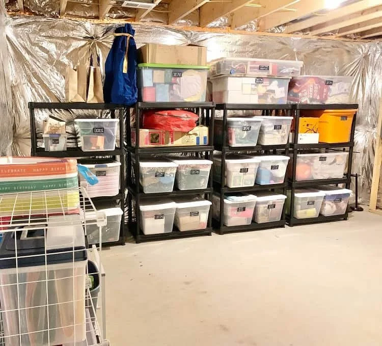 Black shelving units in a basement storing labeled plastic bins arranged by category.