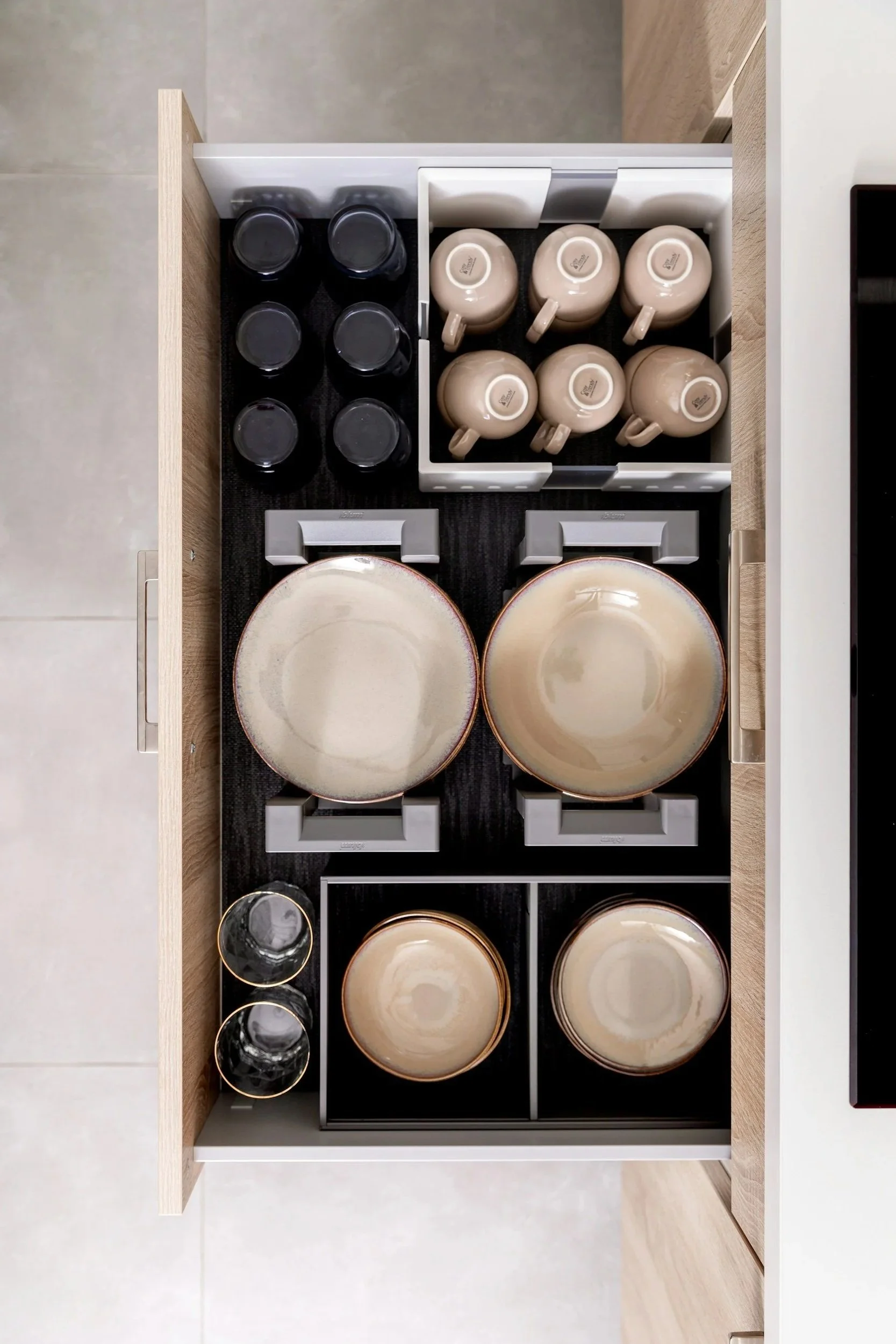 Custom kitchen drawer organization with neatly arranged dishes, mugs, and storage inserts for maximum space efficiency.