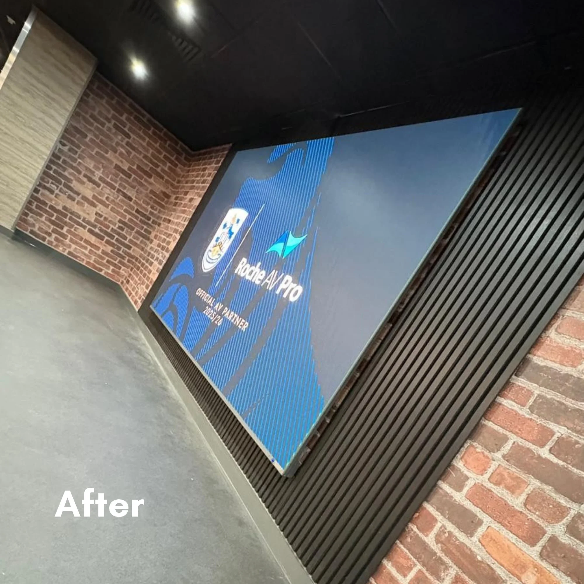 Large digital display screen with Rode AI Pro logo, situated on a wall with brick and wood paneling in an indoor setting.