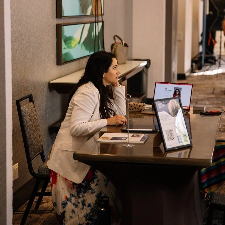 Amy Siegfried is in a white blazer sitting at a table with a laptop and marketing materials in an indoor setting.