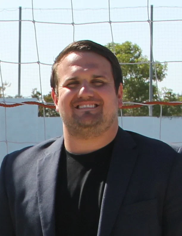 Man in a suit smiling in front of a sports net