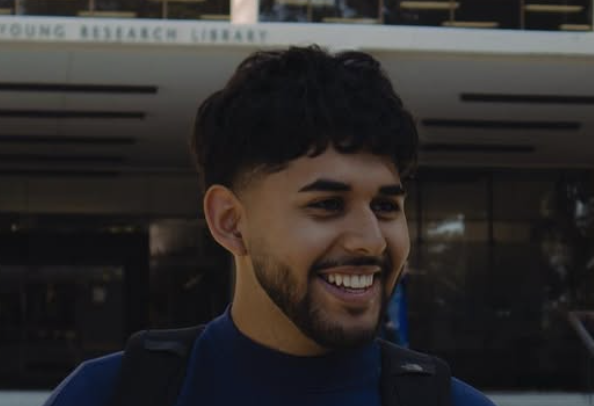 Smiling person in front of a building with a faint sign titled "Young Research Library".