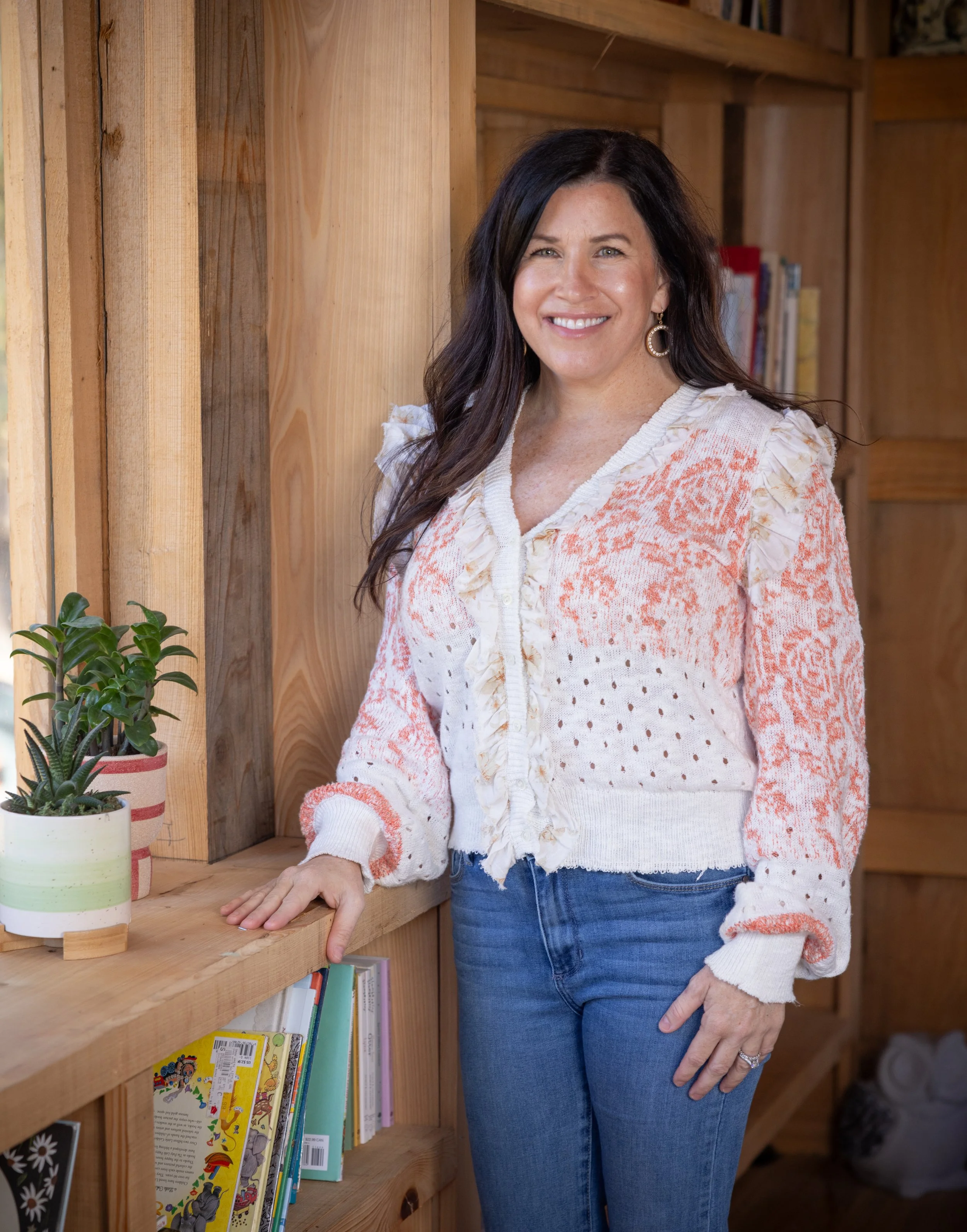 Person smiling indoors next to a window wearing a white paisley shirt