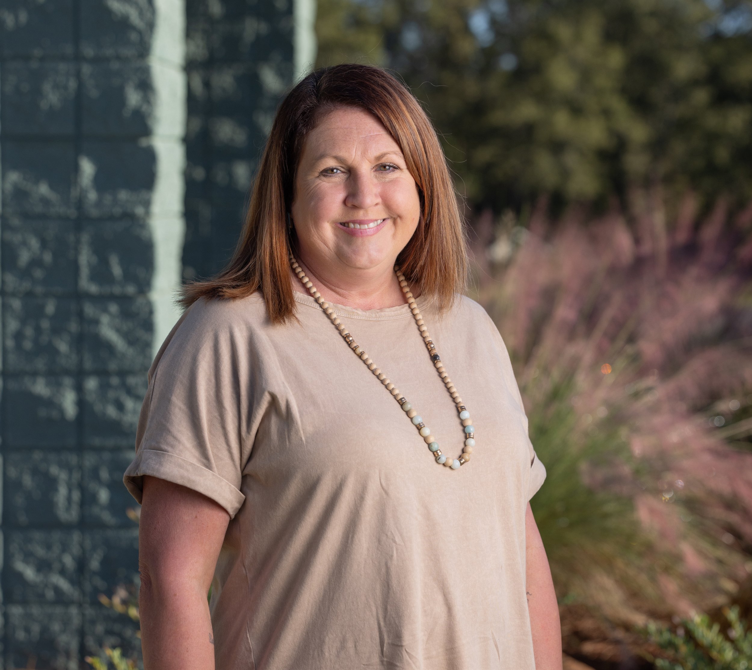 Smiling woman in blue striped shirt indoors, relaxed pose next to table with a wicker lamp.