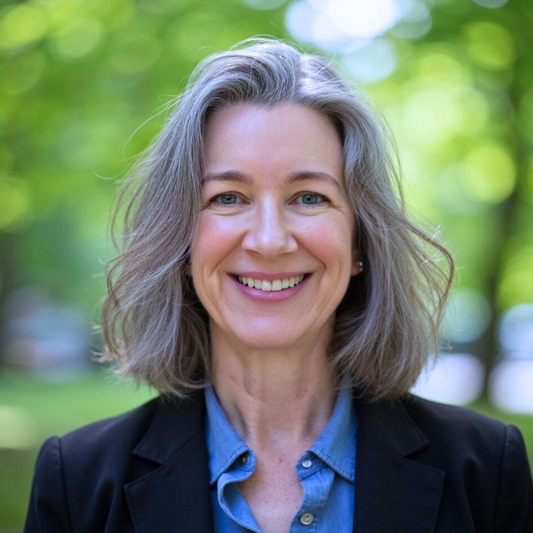 A smiling woman outdoors in a park with trees in the background.