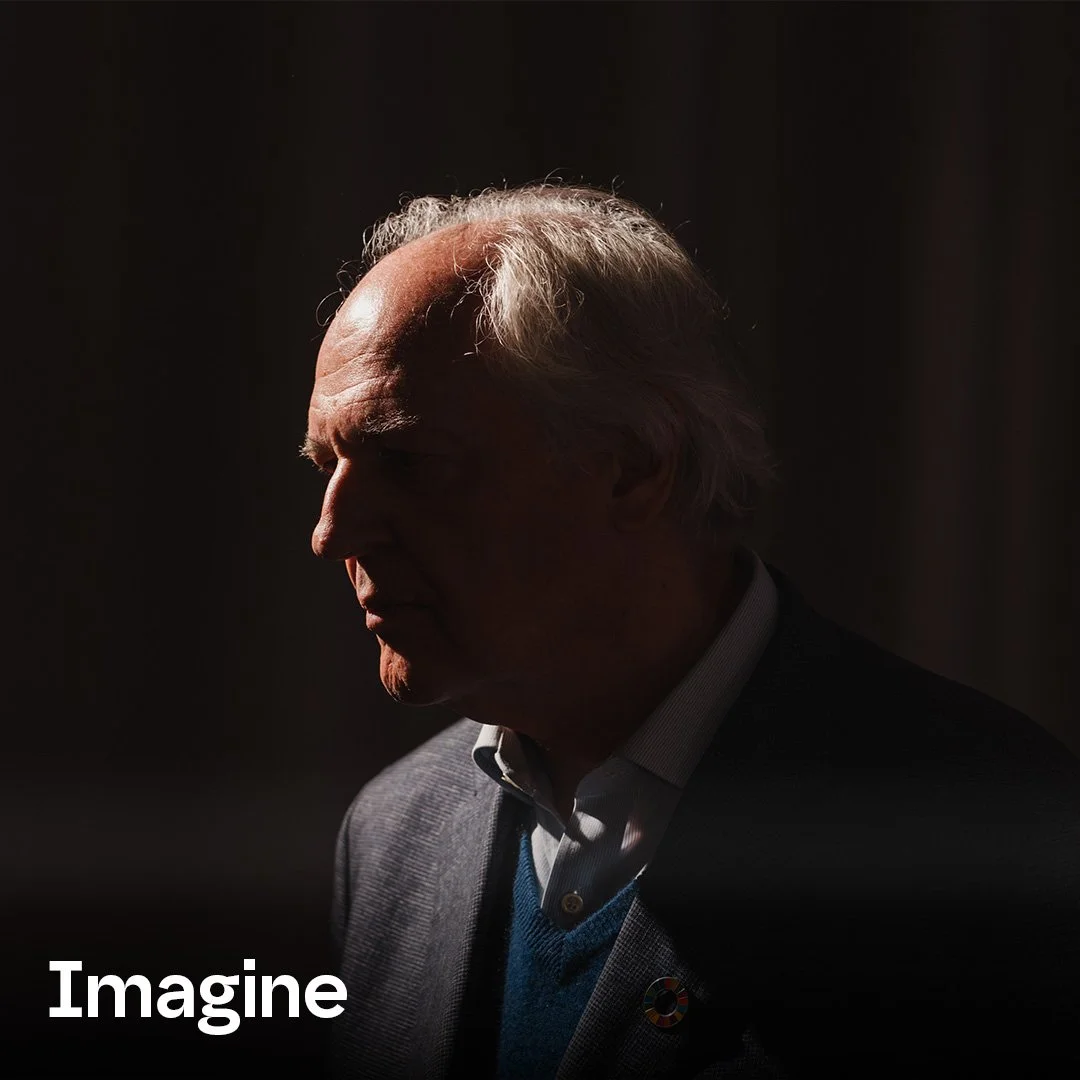 A silhouette of an elderly man with gray hair, wearing a suit and a sweater vest, facing left in a dark background with minimal lighting highlighting his profile.