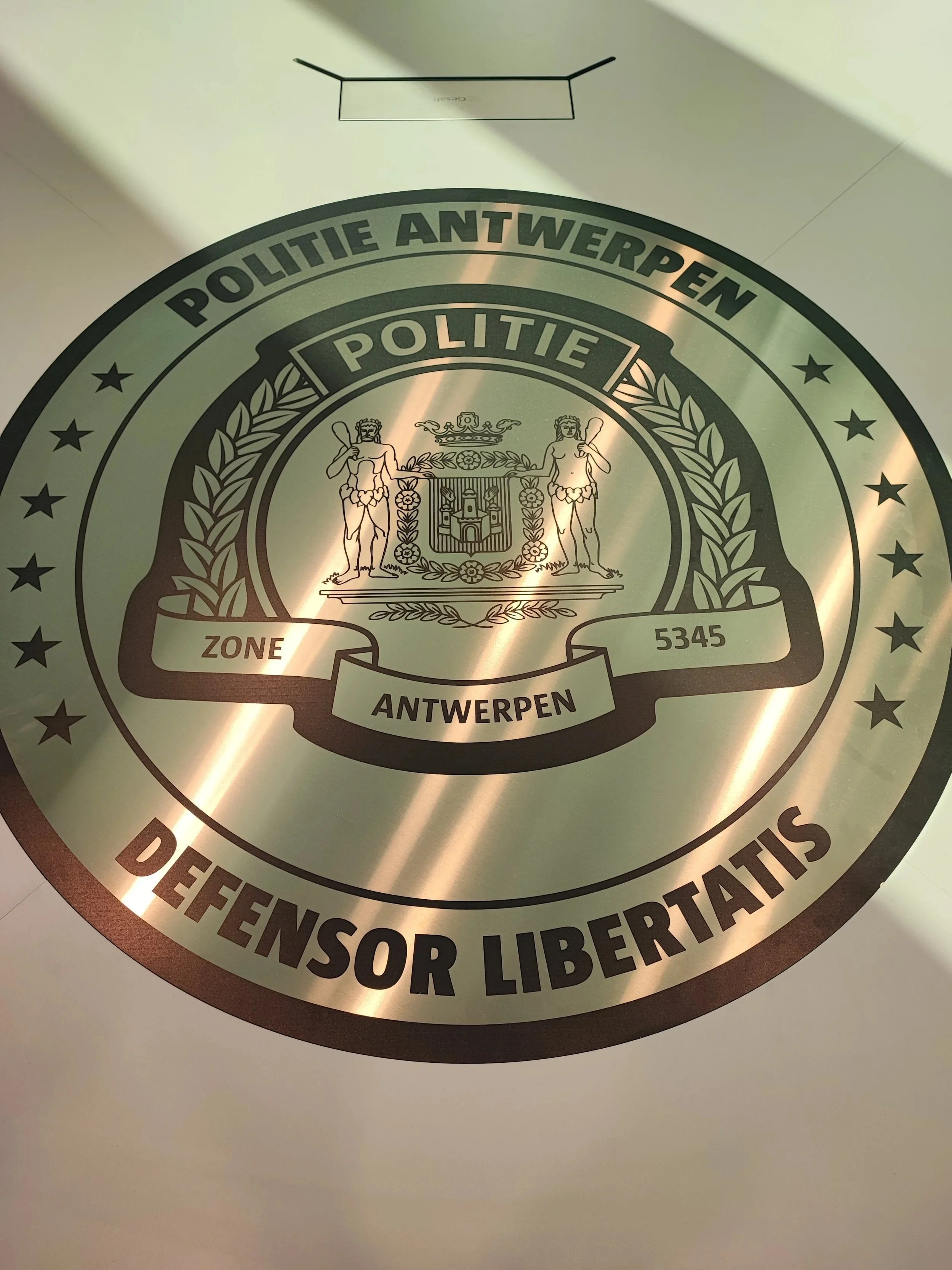 Close-up photo of a seal or badge of the Antwerp police department, featuring the coat of arms and the words "Politie Antwerpen" and "Detectives of Libertatis".