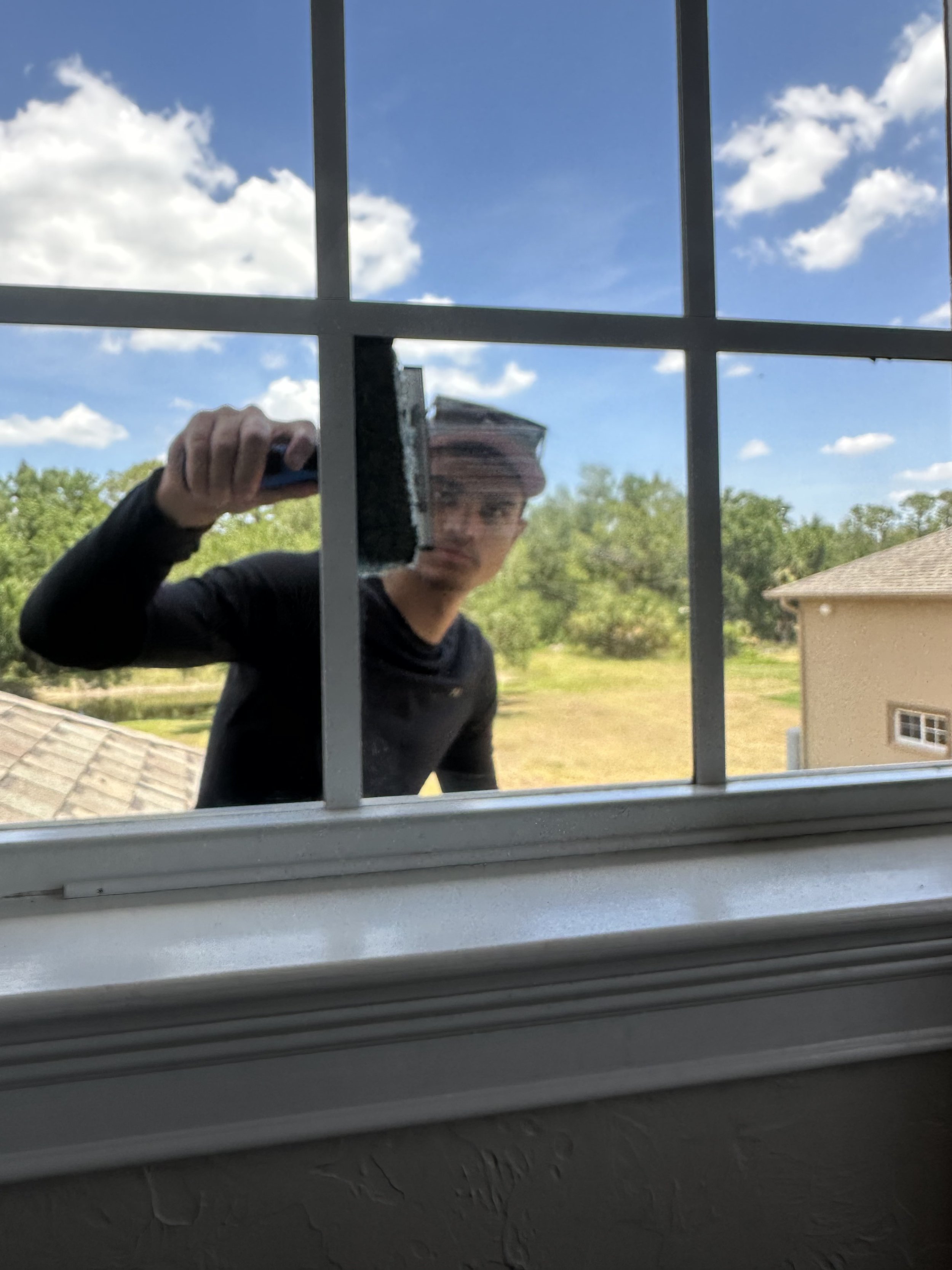 Window cleaner outside window, holding squeegee, clear blue sky with clouds in background. Window Washing.