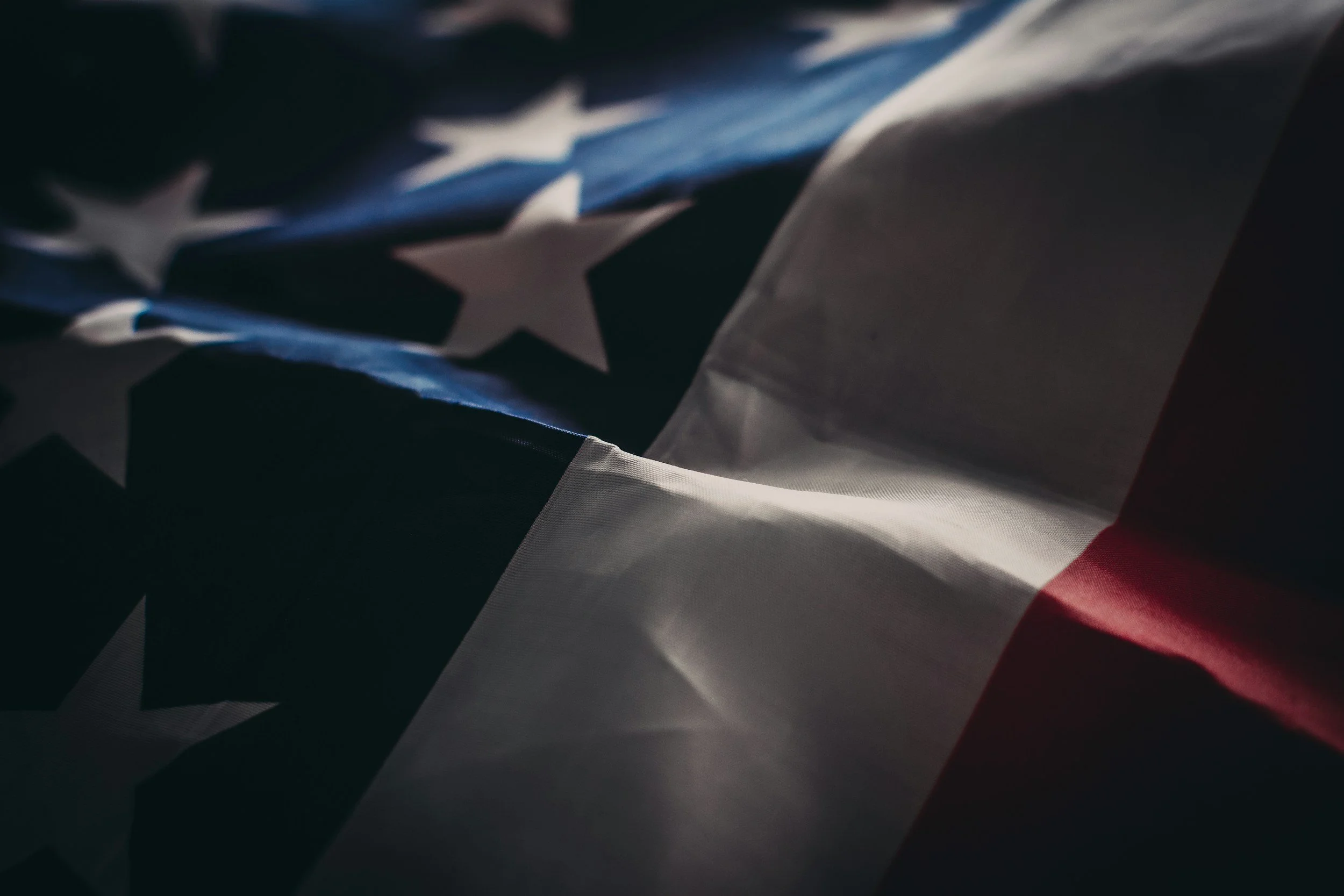 Close-up of a crumpled American flag with stars and stripes, partially illuminated.